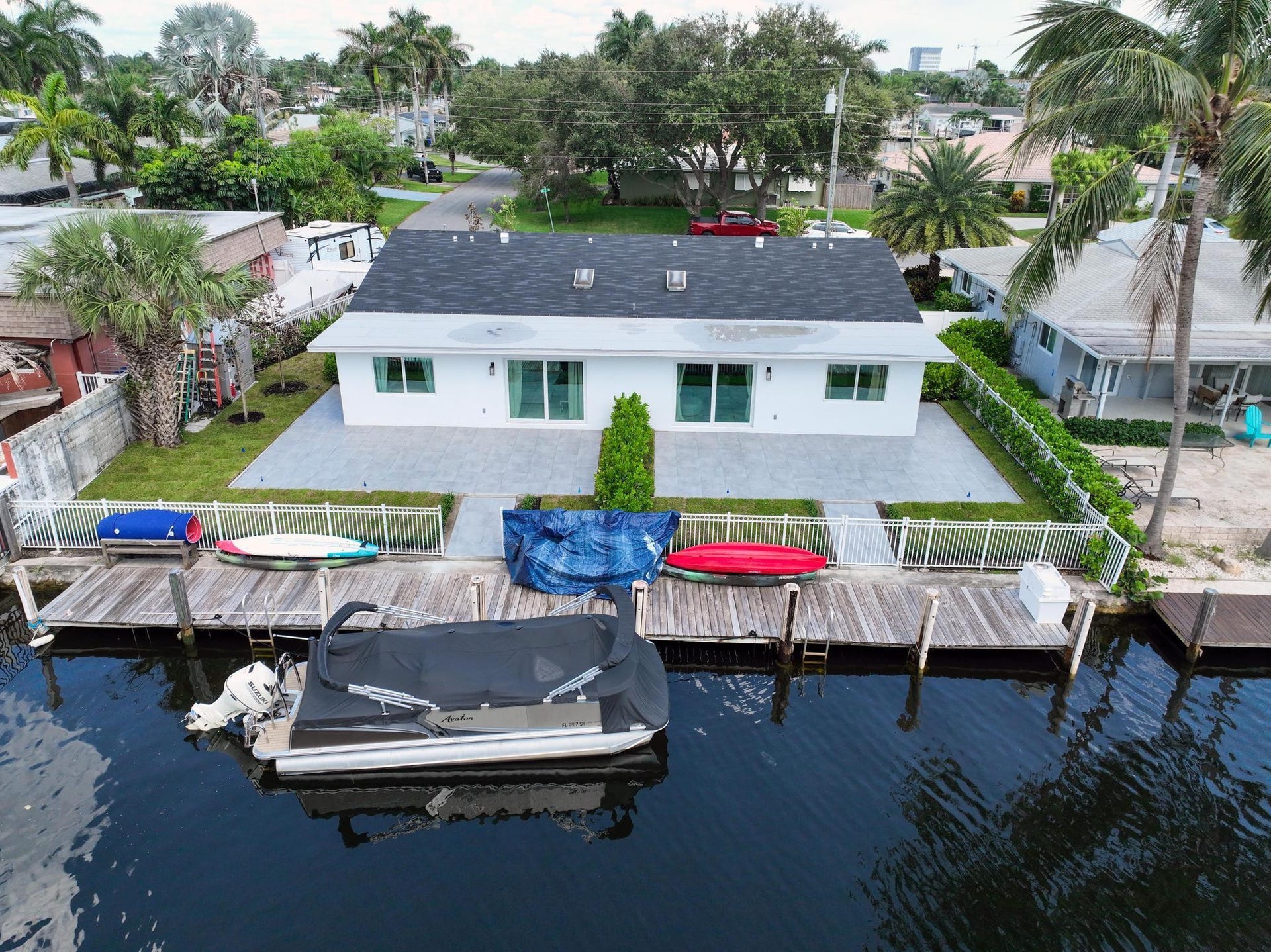 Waterfront property featuring a white exterior, dark shingle roof, expansive paver patio, and private boat dock