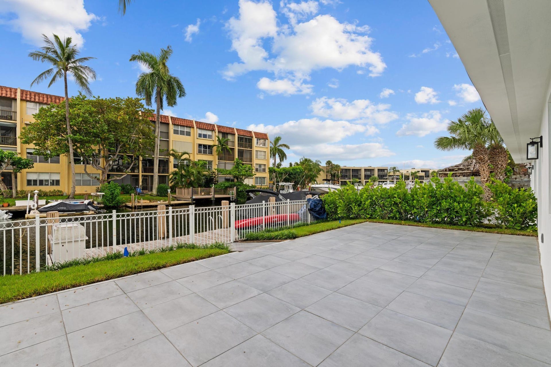 Spacious outdoor patio with large format tile, bordered by a manicured hedge and a white metal fence