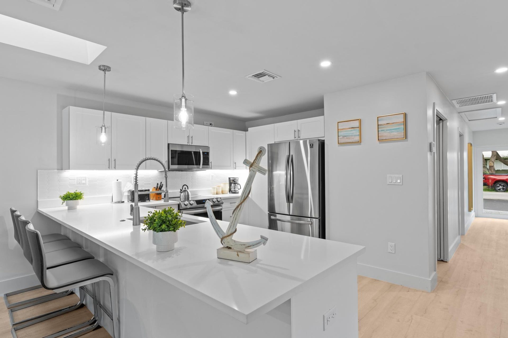 Modern kitchen featuring an expansive island with white countertops, white cabinetry, stainless steel appliances, and wood-finish flooring