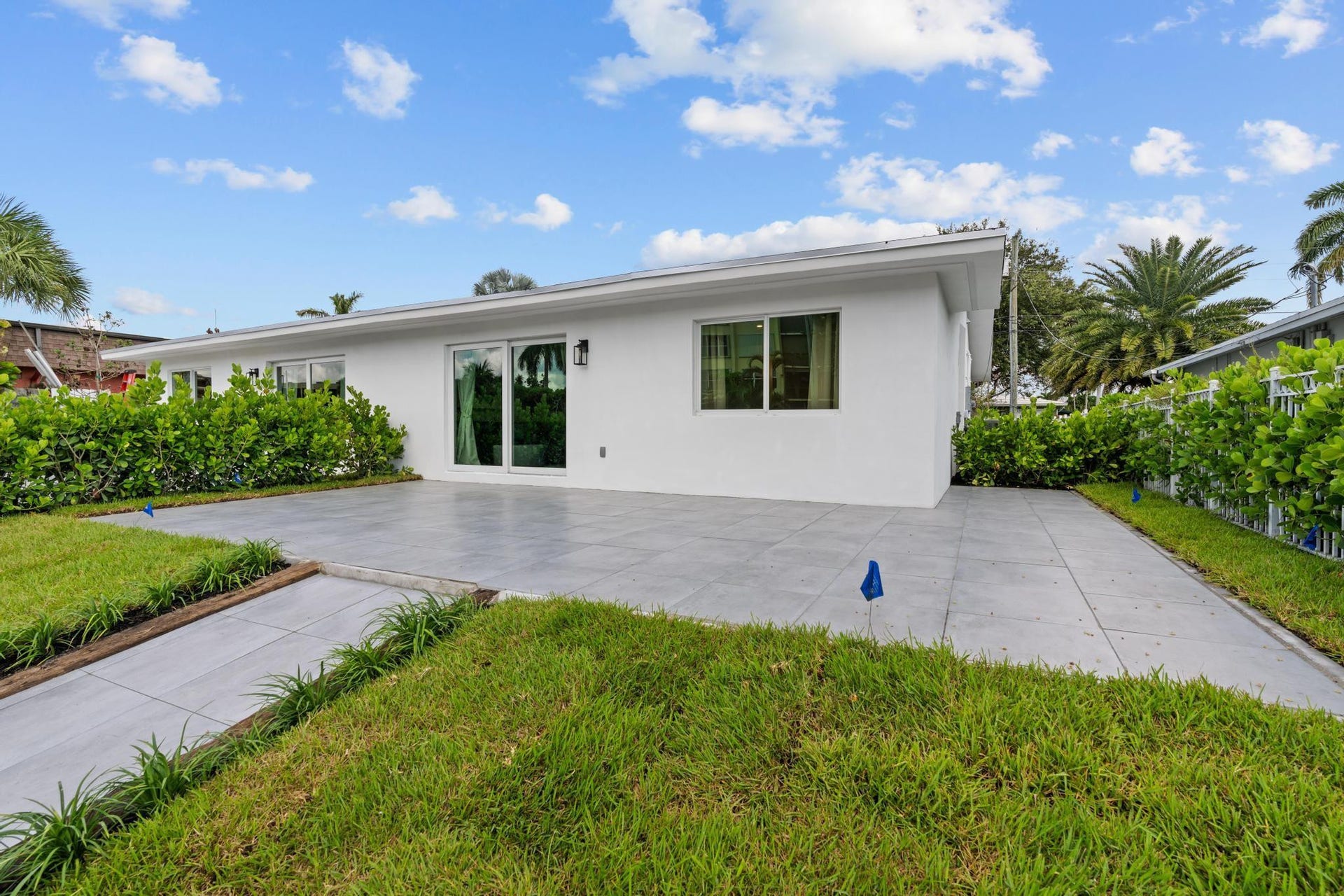 White stucco exterior with sliding glass doors, multiple windows, and a large paver patio