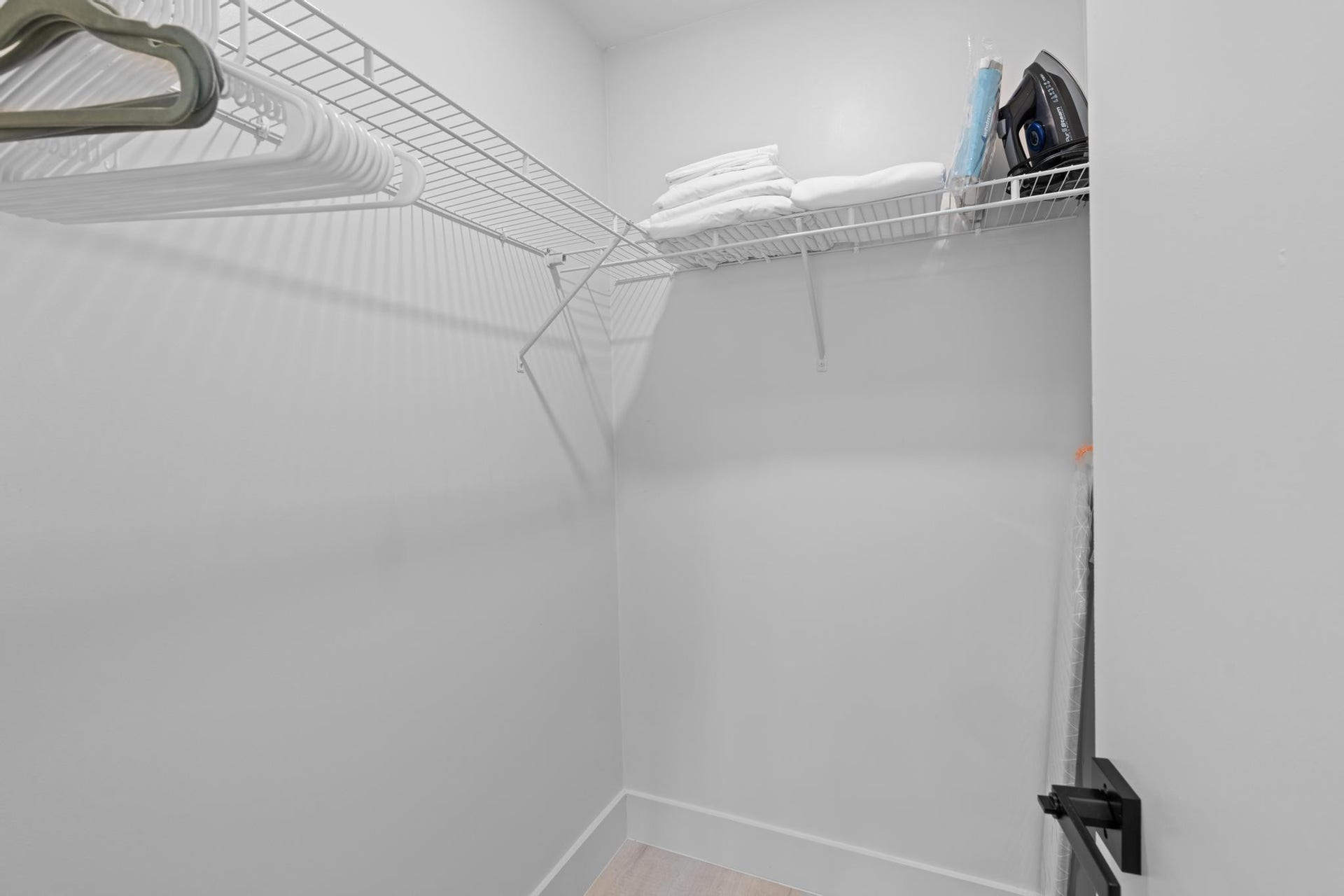 White wire shelving system with hanging rod, light-toned wood-finish flooring, and white walls