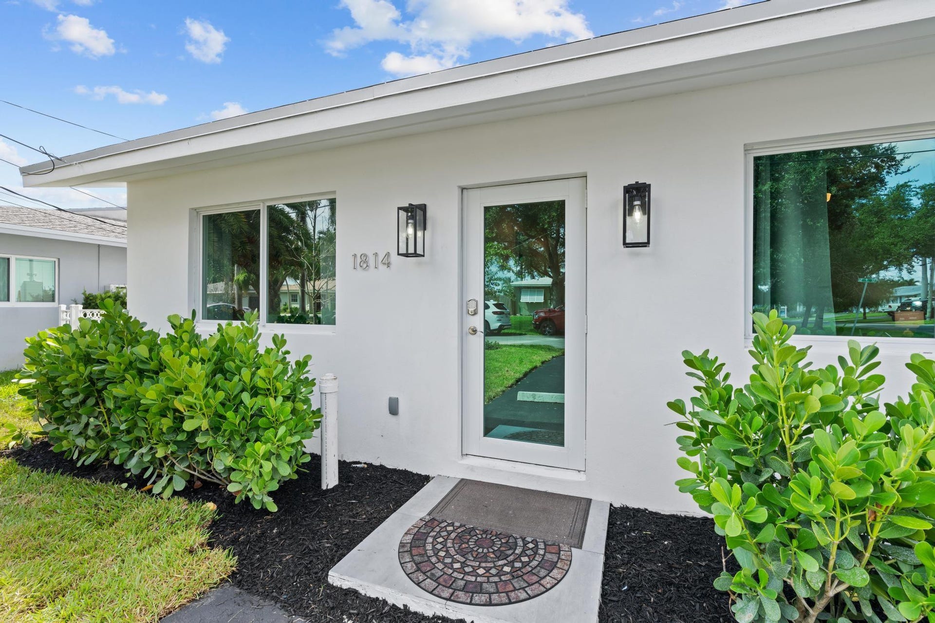 White exterior with modern black-framed outdoor lighting, full-light entry door, and a concrete entry pad with decorative inlay