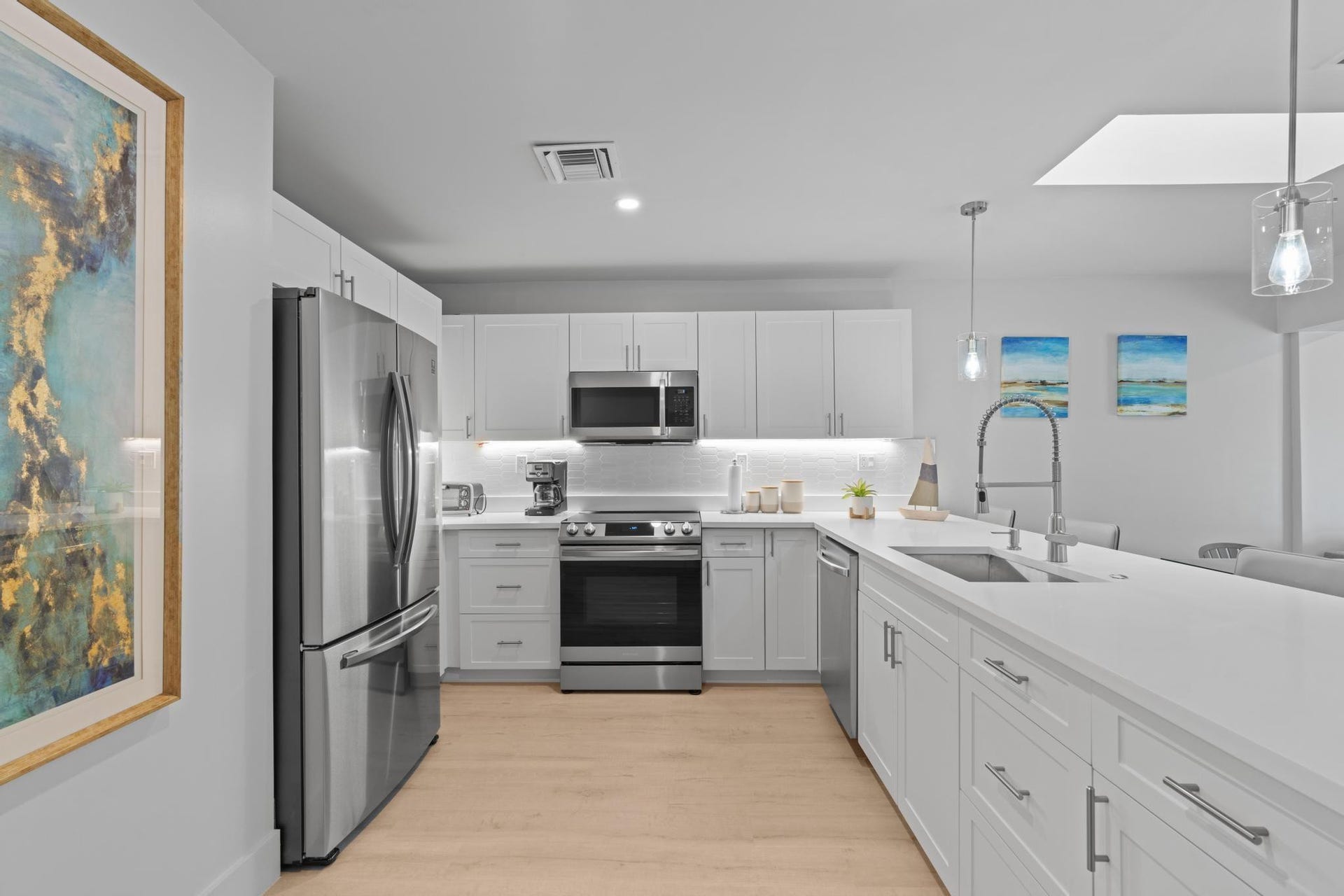 Modern kitchen featuring stainless steel appliances, light wood-finish flooring, white cabinetry, a large kitchen island with an undermount sink, and recessed lighting