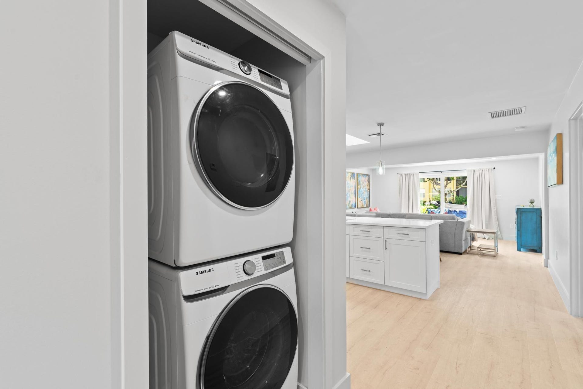 Stackable laundry appliances in a dedicated alcove, wood-finish flooring, white kitchen island with cabinetry, recessed lighting, and patio doors