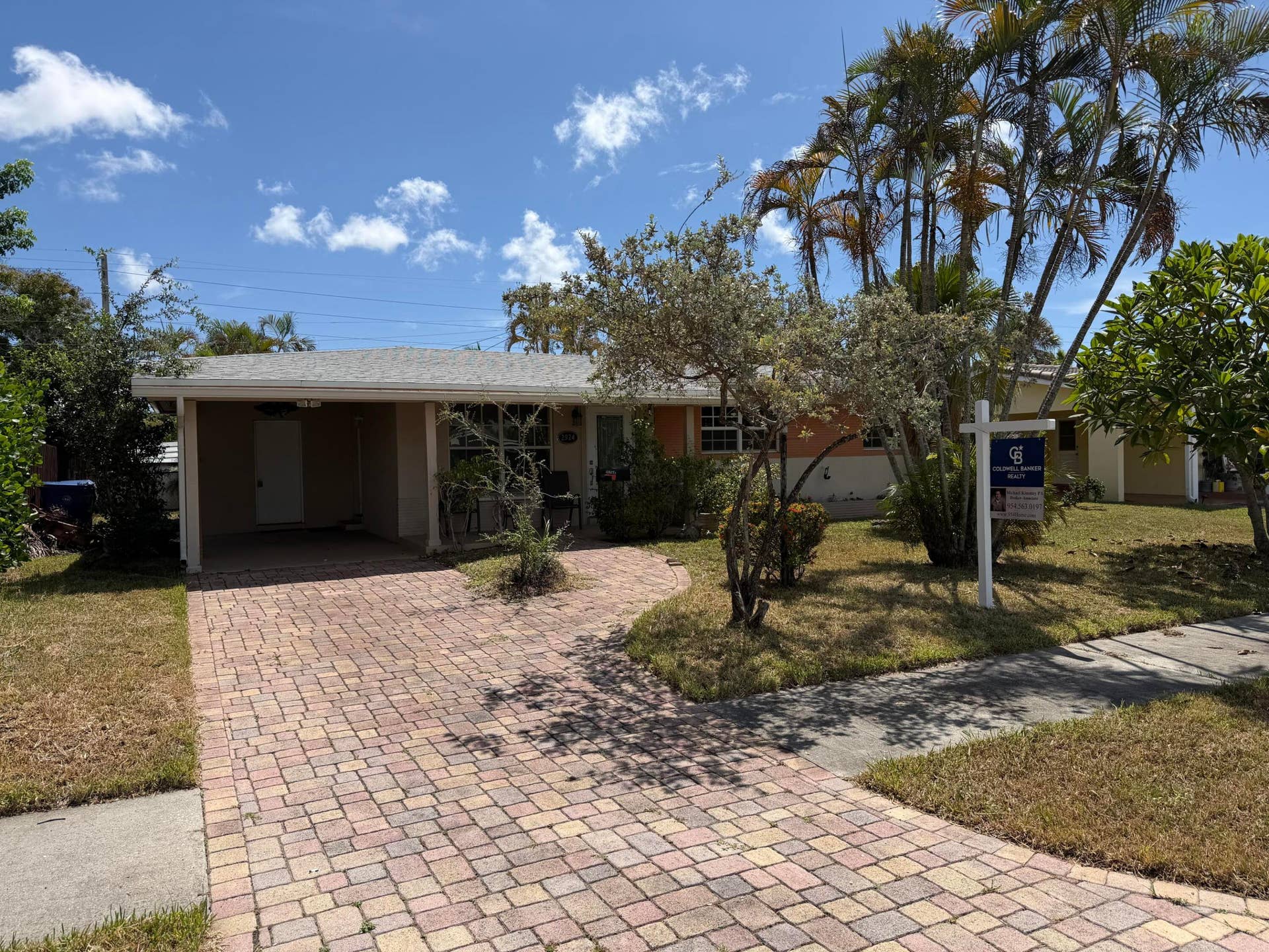 2924 NW 9TH Terrace, Wilton Manors, FL 33311 Single-story residence featuring a covered carport, brick paver driveway, and mature palm trees