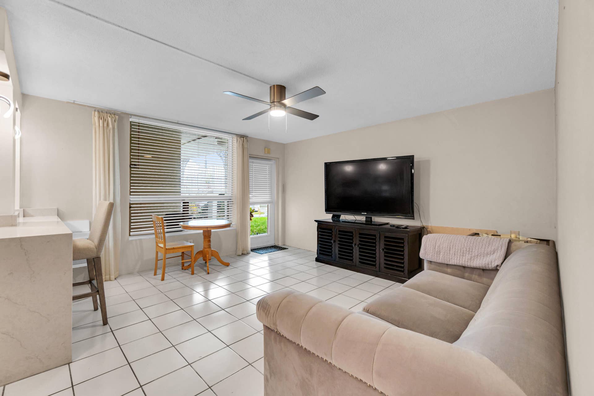 2840 NE 33RD Court, #2, Fort Lauderdale, FL 33306 White tile flooring, ceiling fan, built-in breakfast bar with stone-finish countertop, large window with blinds, and glass-paneled exterior door