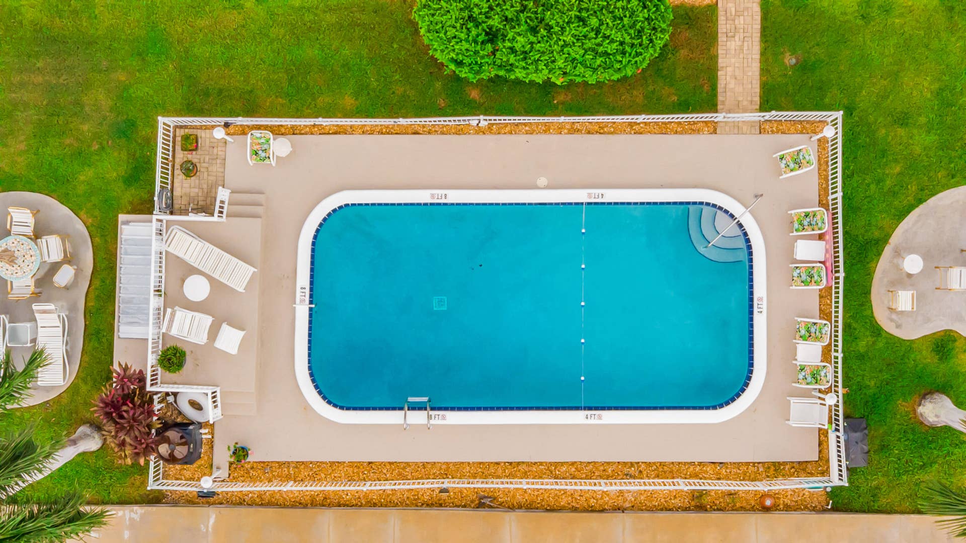 2840 NE 33RD Court, #2, Fort Lauderdale, FL 33306 Rectangular swimming pool with integrated steps, surrounded by a paved deck, white fencing, and landscaped greenery