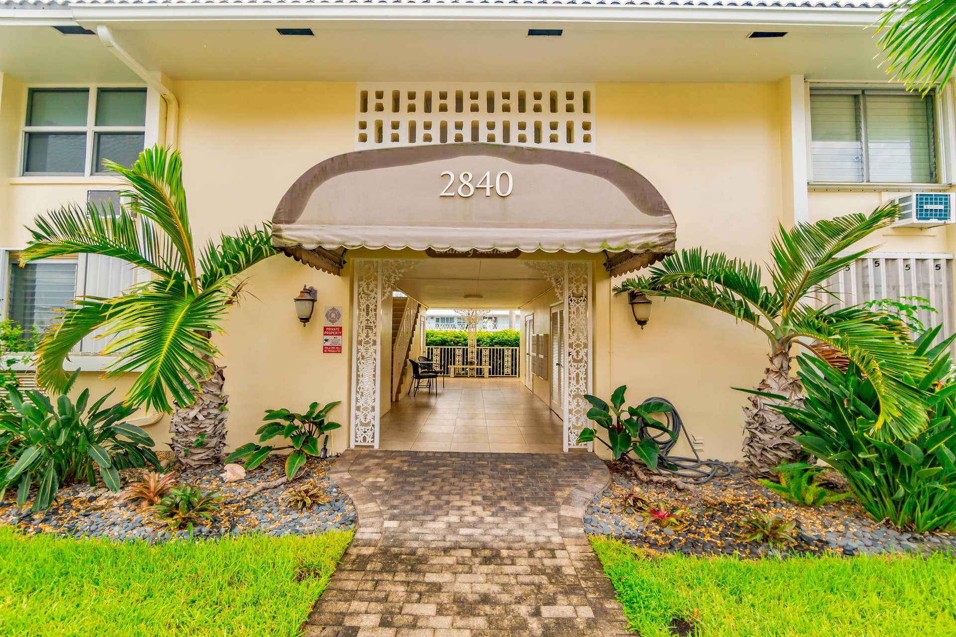 2840 NE 33RD Court, #2, Fort Lauderdale, FL 33306 Building exterior with a covered entry, featuring a paved walkway, manicured lawn, and tropical landscaping