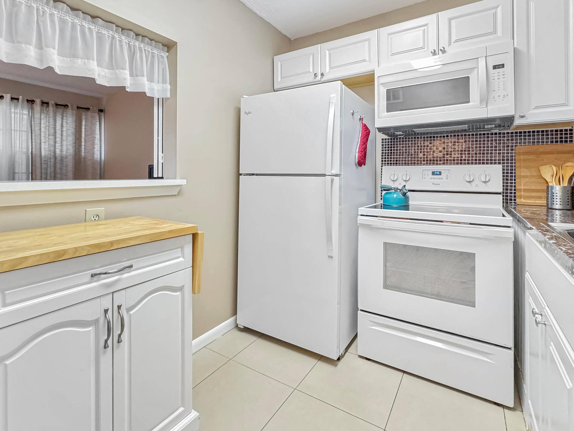 1013 HARWOOD C, #1013, Deerfield Beach, FL 33442 Kitchen featuring white cabinetry, tile flooring, mosaic tile backsplash, and a pass-through window