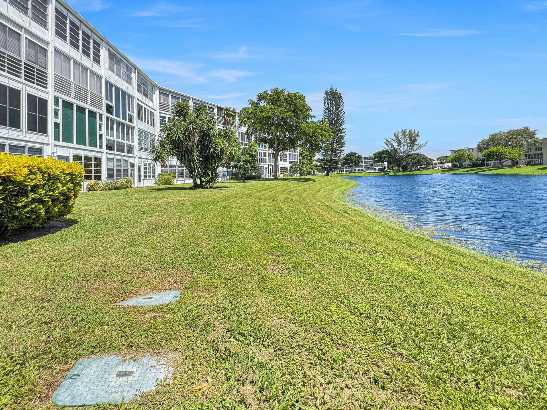 1013 HARWOOD C, #1013, Deerfield Beach, FL 33442 Expansive lawn area with established landscaping, bordering a serene water feature