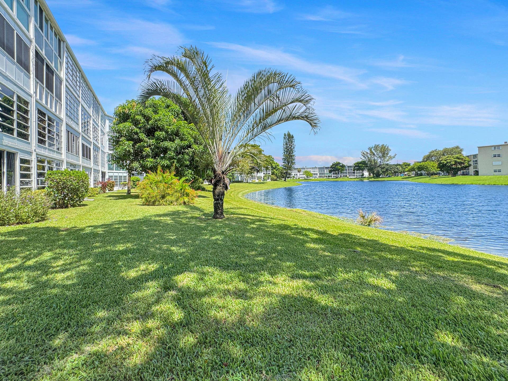 1013 HARWOOD C, #1013, Deerfield Beach, FL 33442 Lakeside building with multiple windows, surrounded by green lawns, mature palm trees, and established landscaping