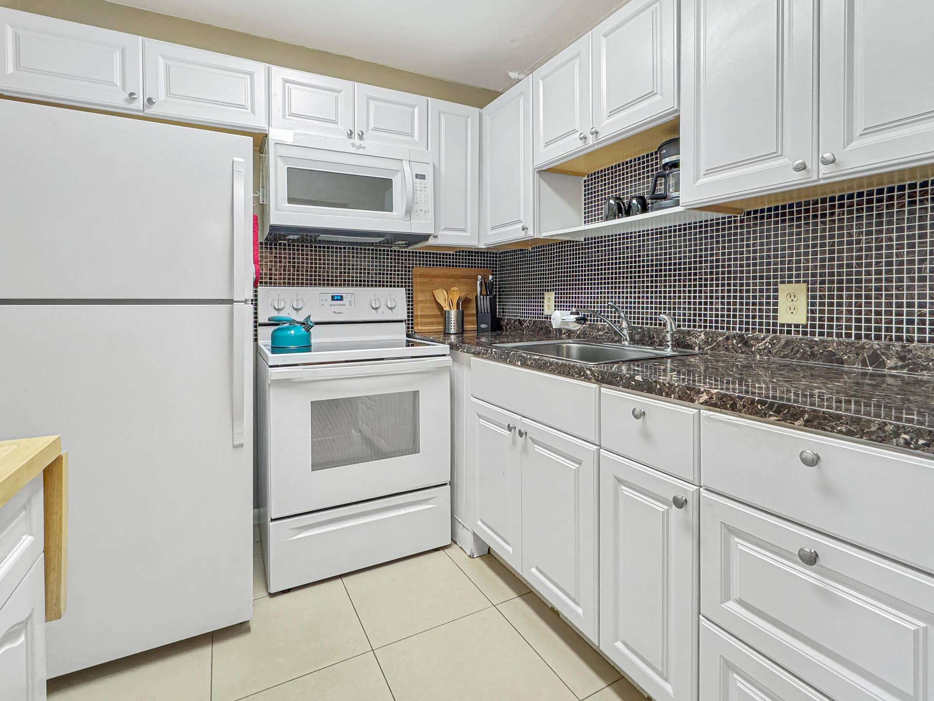 1013 HARWOOD C, #1013, Deerfield Beach, FL 33442 White cabinetry with brushed nickel hardware, dark mosaic tile backsplash, solid surface countertops, and white appliances