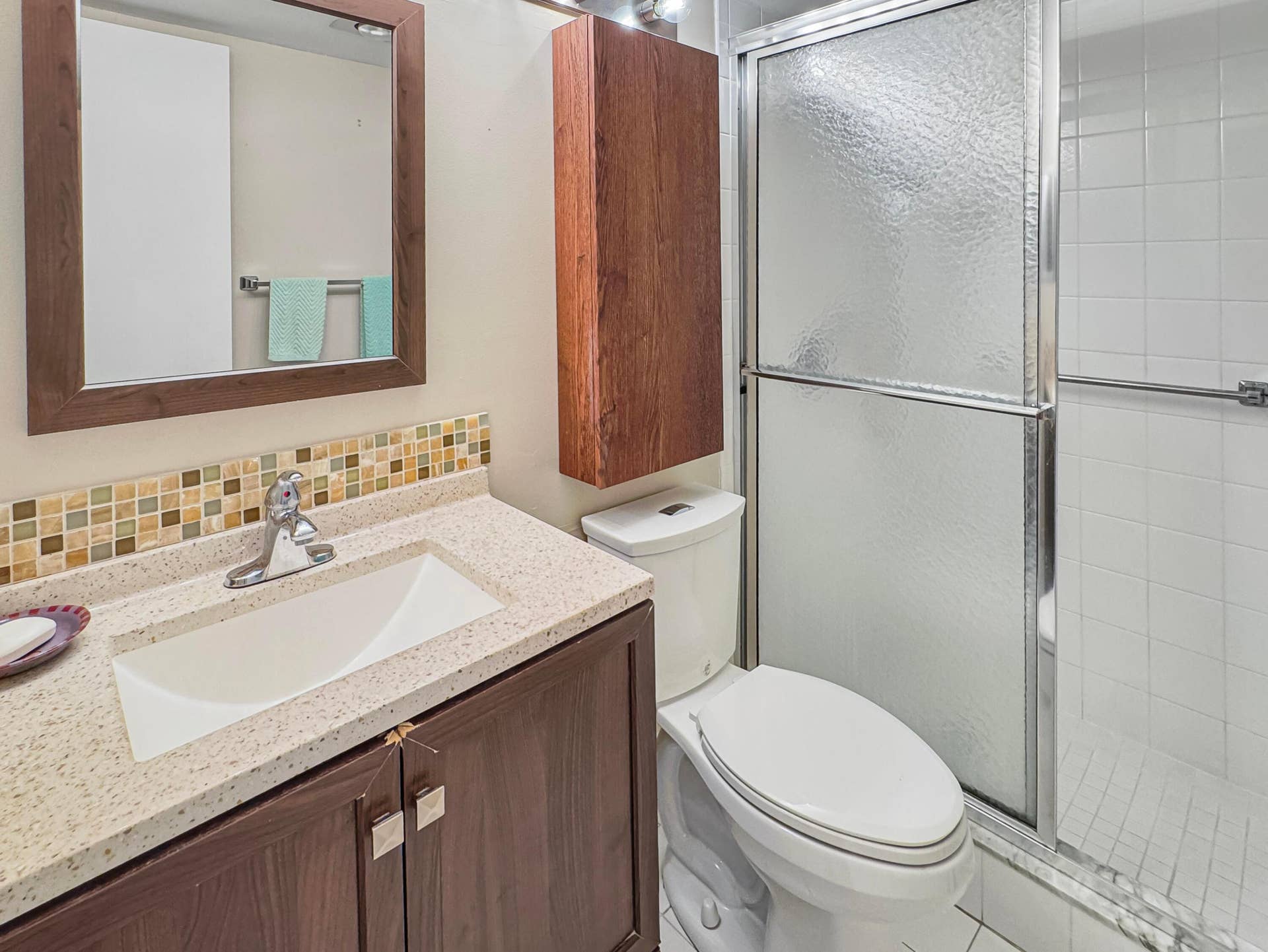 1013 HARWOOD C, #1013, Deerfield Beach, FL 33442 Bathroom featuring a vanity with an integrated sink, mosaic tile backsplash, wood-finish cabinetry, and a shower with sliding glass doors