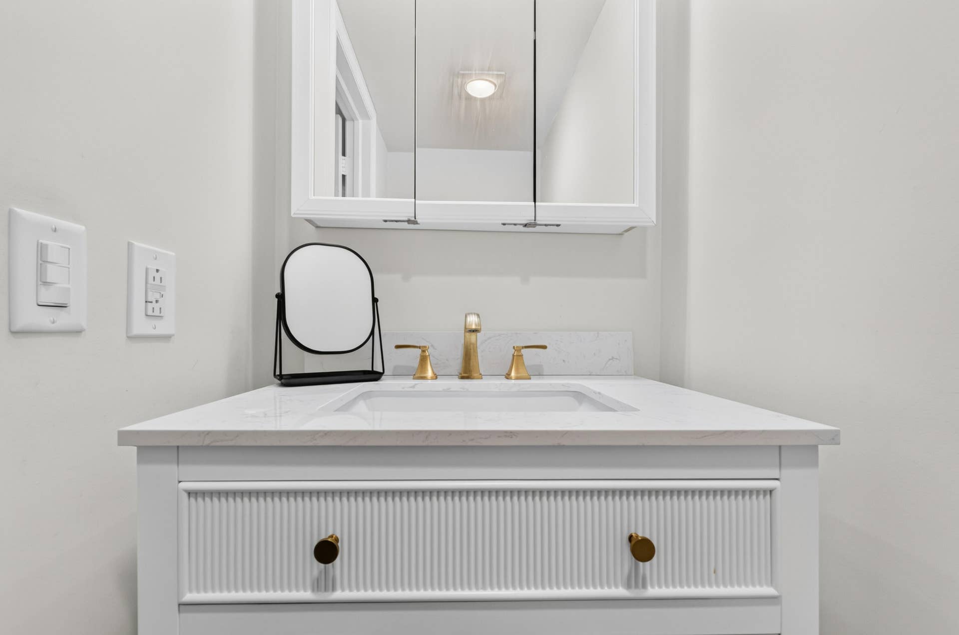 6359 Bay Club Drive, #2, Fort Lauderdale, FL 33308 Elegant bathroom vanity featuring a white ribbed cabinetry base with brass hardware, a light stone countertop, and a polished brass three-hole faucet
