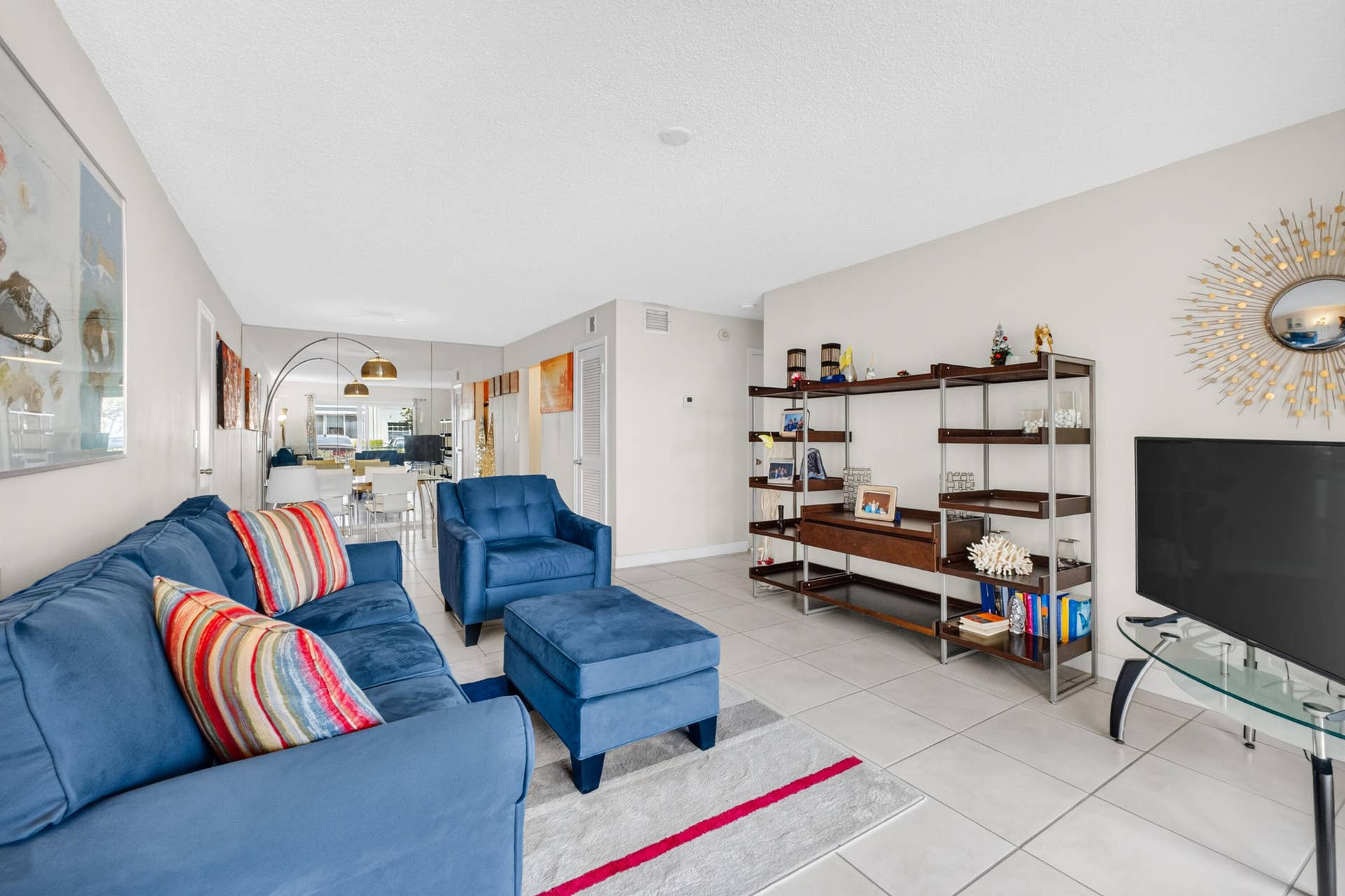 6359 Bay Club Drive, #2, Fort Lauderdale, FL 33308 Open-concept living area featuring tile flooring, abundant natural light from multiple windows, built-in shelving with wood-finish frames, and a flat-screen television mounted above a media console
