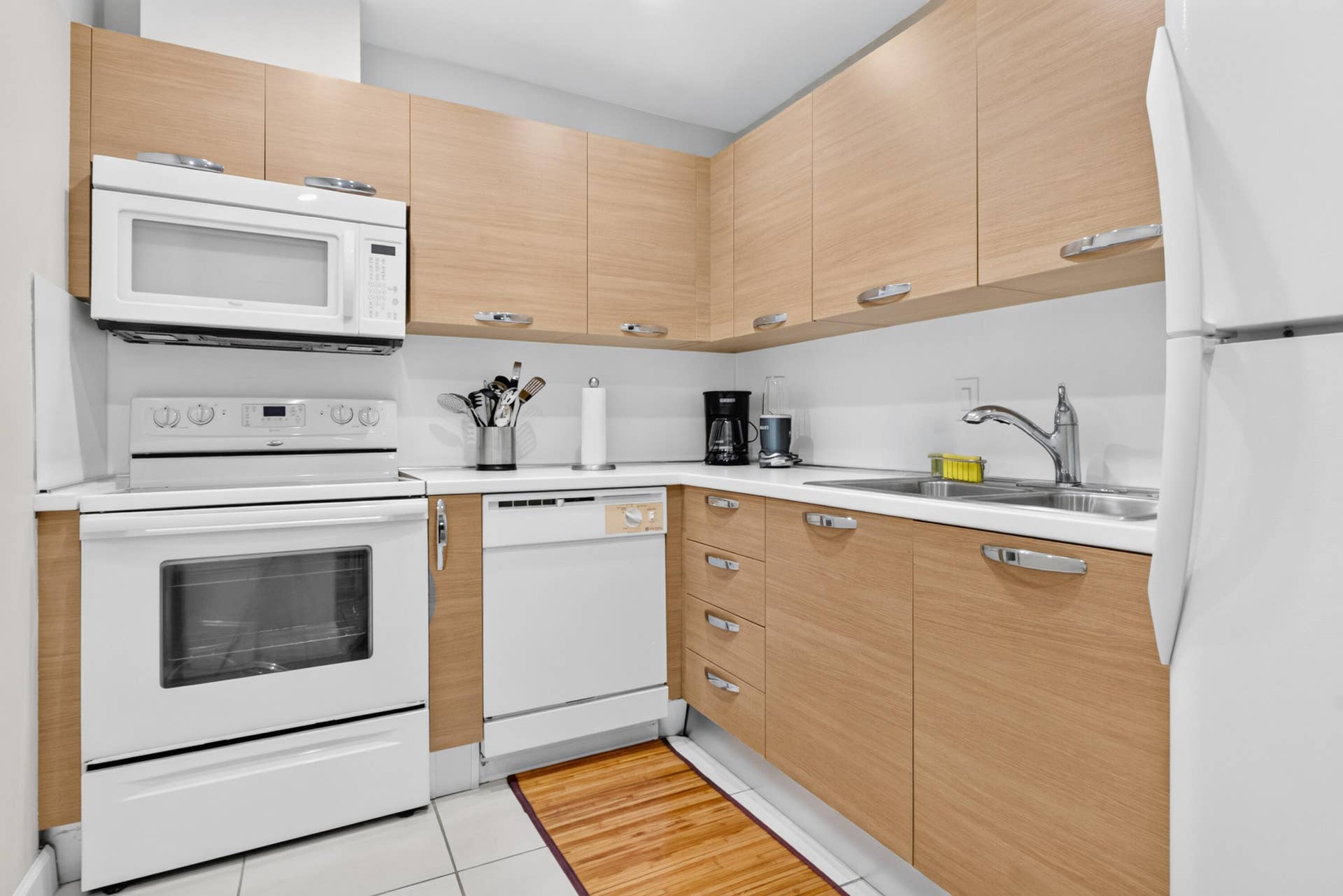 6359 Bay Club Drive, #2, Fort Lauderdale, FL 33308 U-shaped kitchen featuring light wood-finish cabinetry with silver-tone hardware, white countertops, and white appliances including a built-in microwave, range, and dishwasher