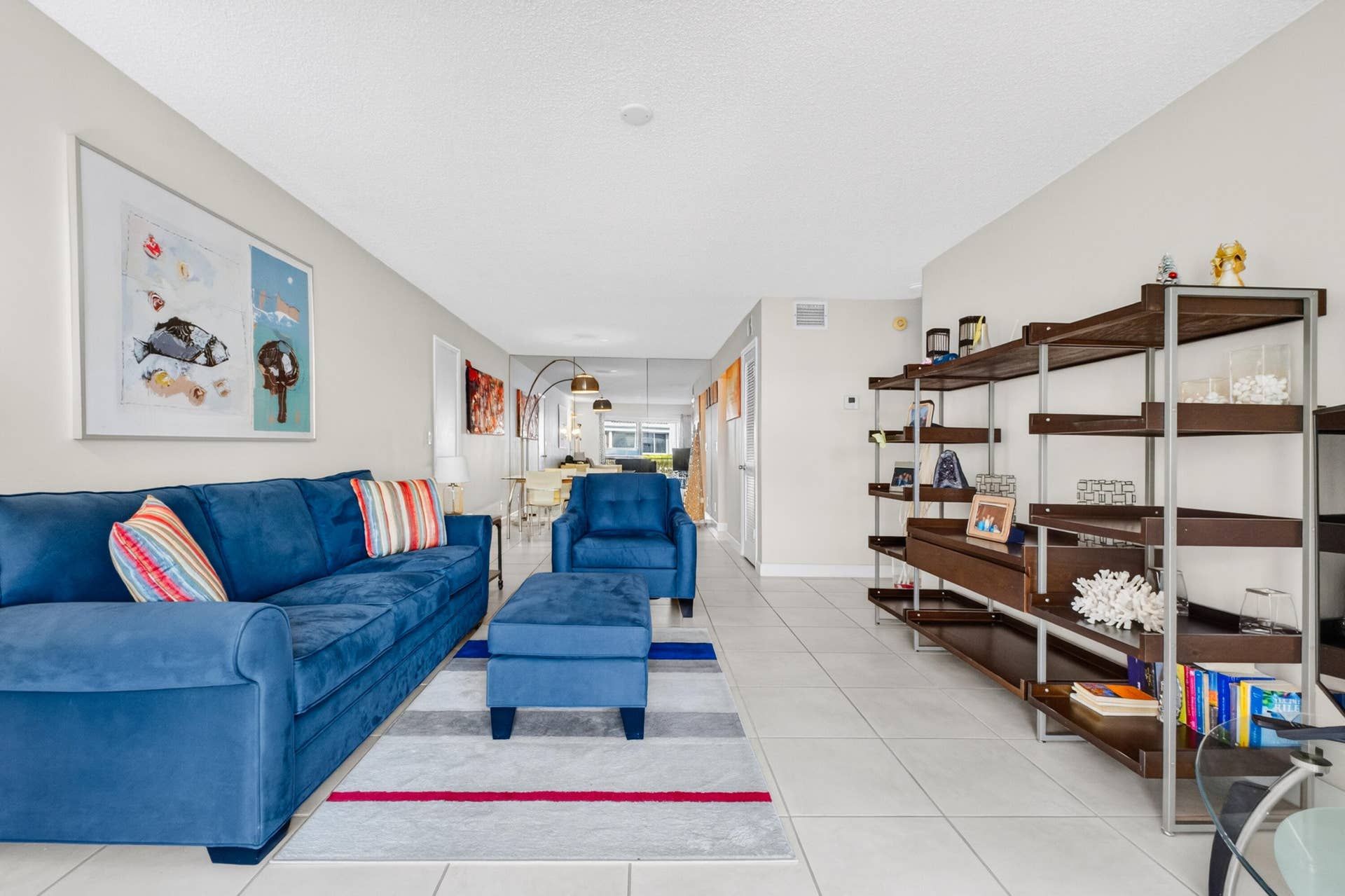 6359 Bay Club Drive, #2, Fort Lauderdale, FL 33308 Bright, open-concept living area featuring tile flooring throughout, custom wood-finish shelving with ample display and storage capacity, and a vibrant blue upholstered sofa anchoring the space