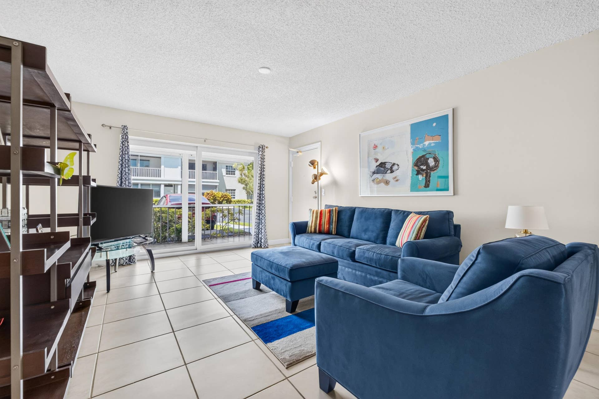 6359 Bay Club Drive, #2, Fort Lauderdale, FL 33308 Bright, open living area featuring tile flooring, built-in shelving with dark wood-finish cabinetry, and glass sliding doors opening to a balcony with city views