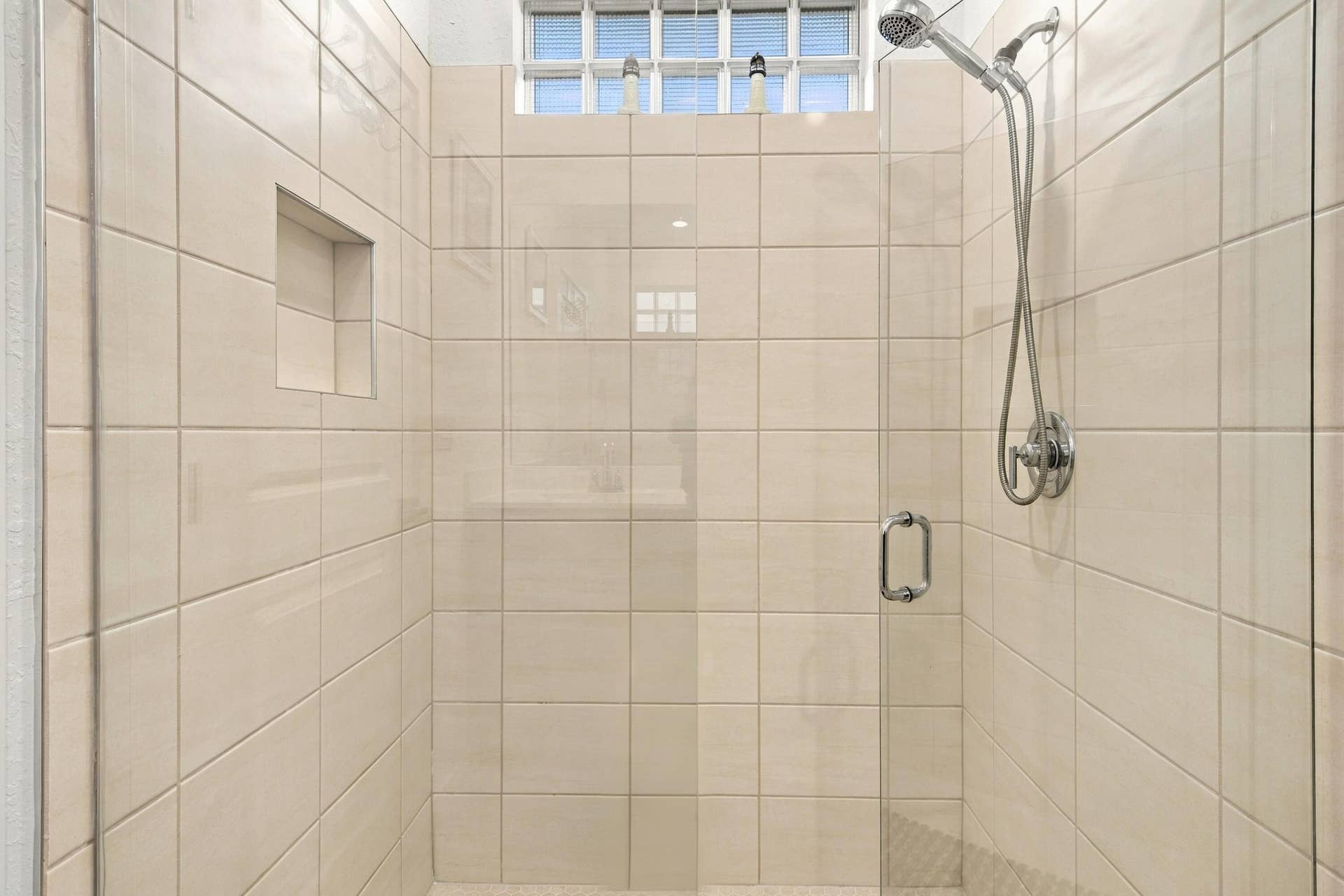 Primary bathroom shower with glass shower doors, ceramic tiles and window