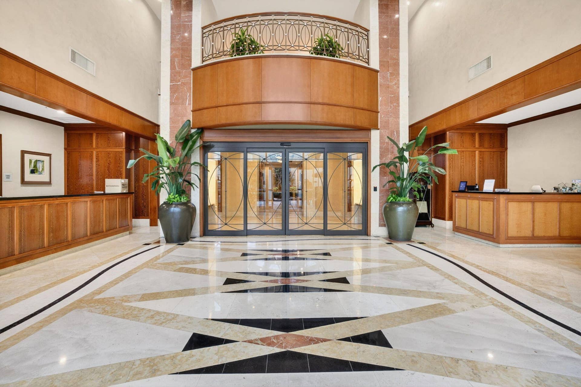Grand two-story lobby featuring a patterned tile floor, wood-paneled walls, and a decorative wrought-iron balcony