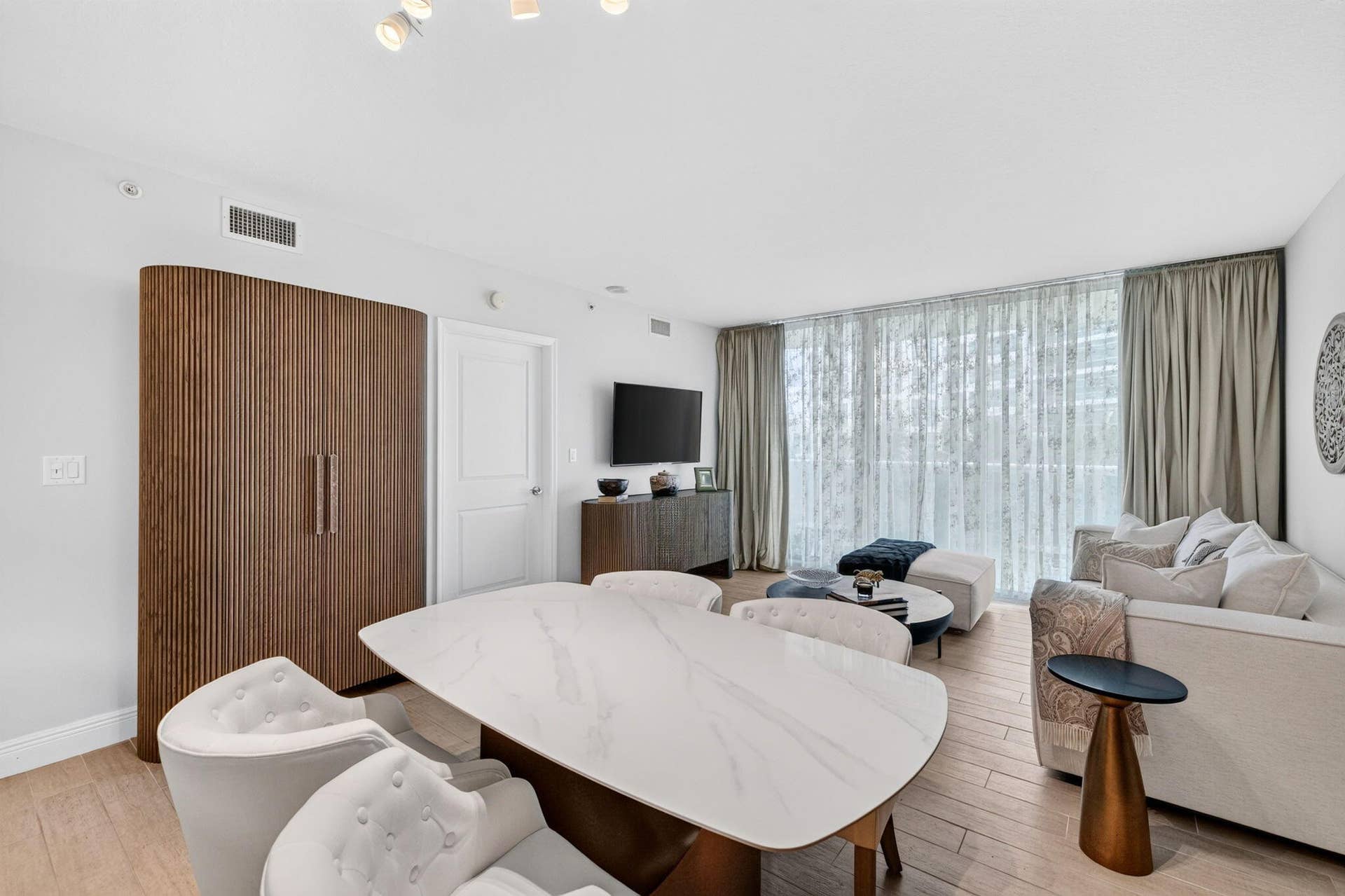 Tile-finish flooring, full-height windows, a built-in slatted wood-paneled cabinet, recessed lighting, and a white interior door