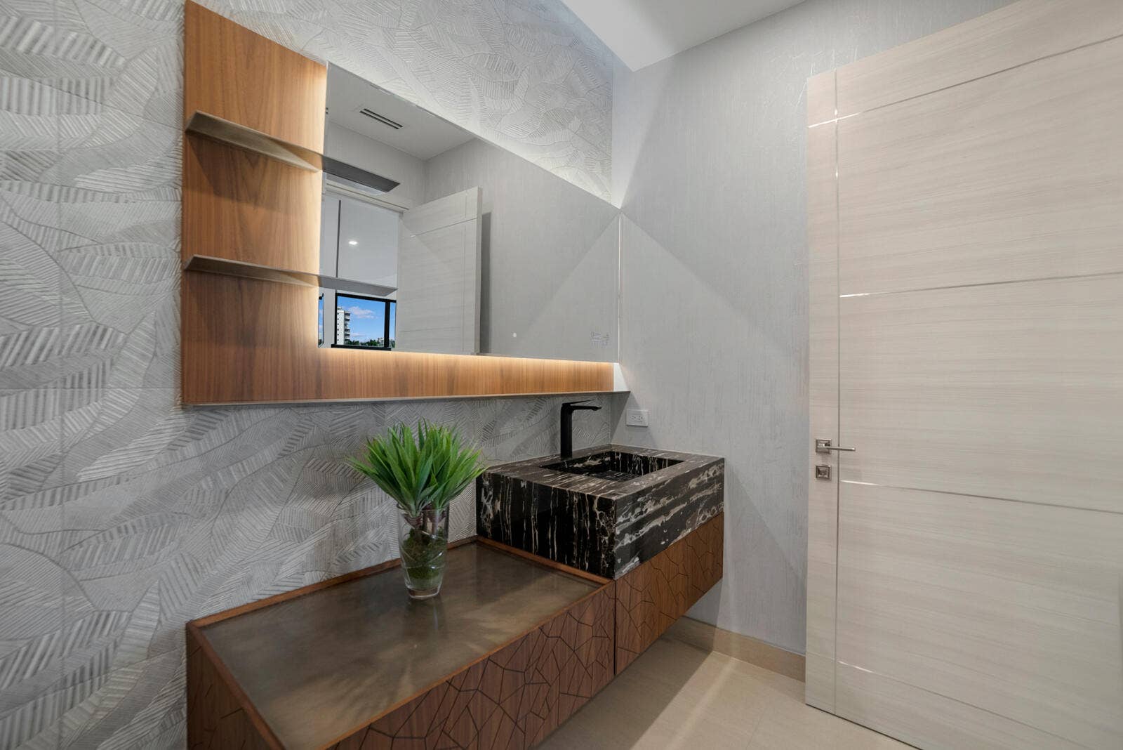414 ROYAL PLAZA Drive, Fort Lauderdale, FL 33301 Sophisticated first-floor powder room featuring a dramatic stone vessel sink, floating custom vanity, textured designer wallcovering, and an illuminated oversized mirror.