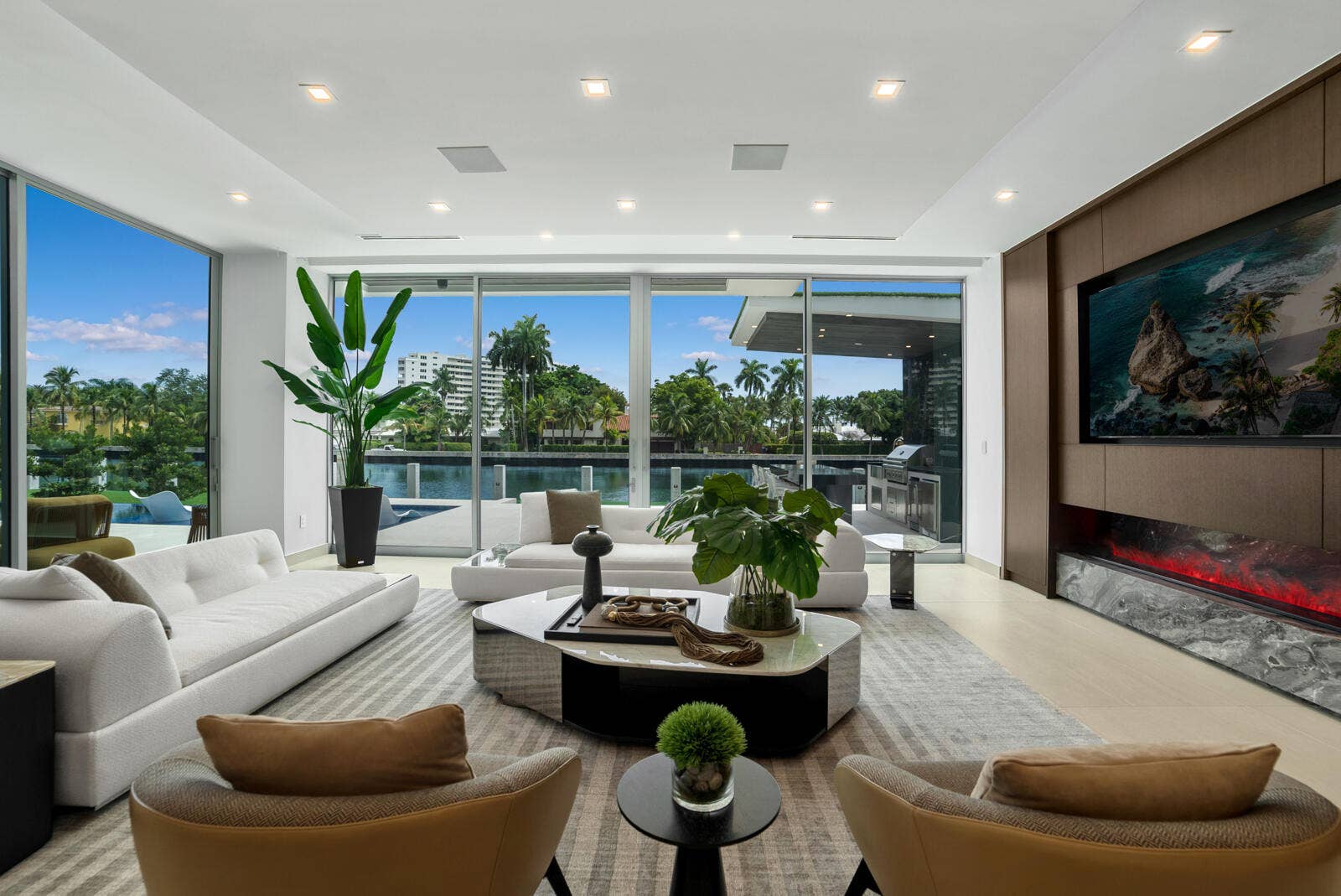 414 ROYAL PLAZA Drive, Fort Lauderdale, FL 33301 Waterfront family and TV room with custom millwork, a built-in television, linear fireplace with dramatic natural-stone surround, and floor-to-ceiling glass opening to the resort-style outdoor living area.