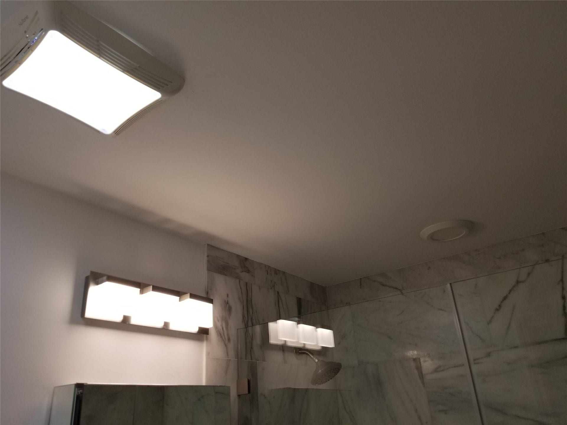 White ceiling with a rectangular flush-mount light fixture, a round recessed light, and wall-mounted vanity lighting