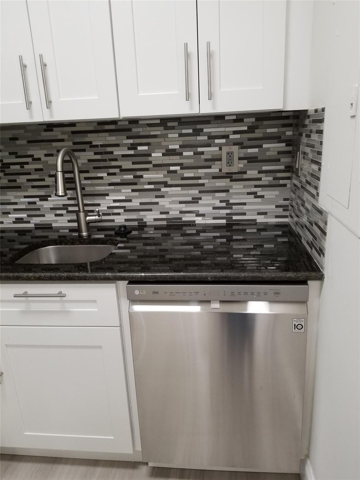 White shaker cabinetry, black granite-style countertop, stainless steel dishwasher, mosaic tile backsplash, and a contemporary gooseneck faucet