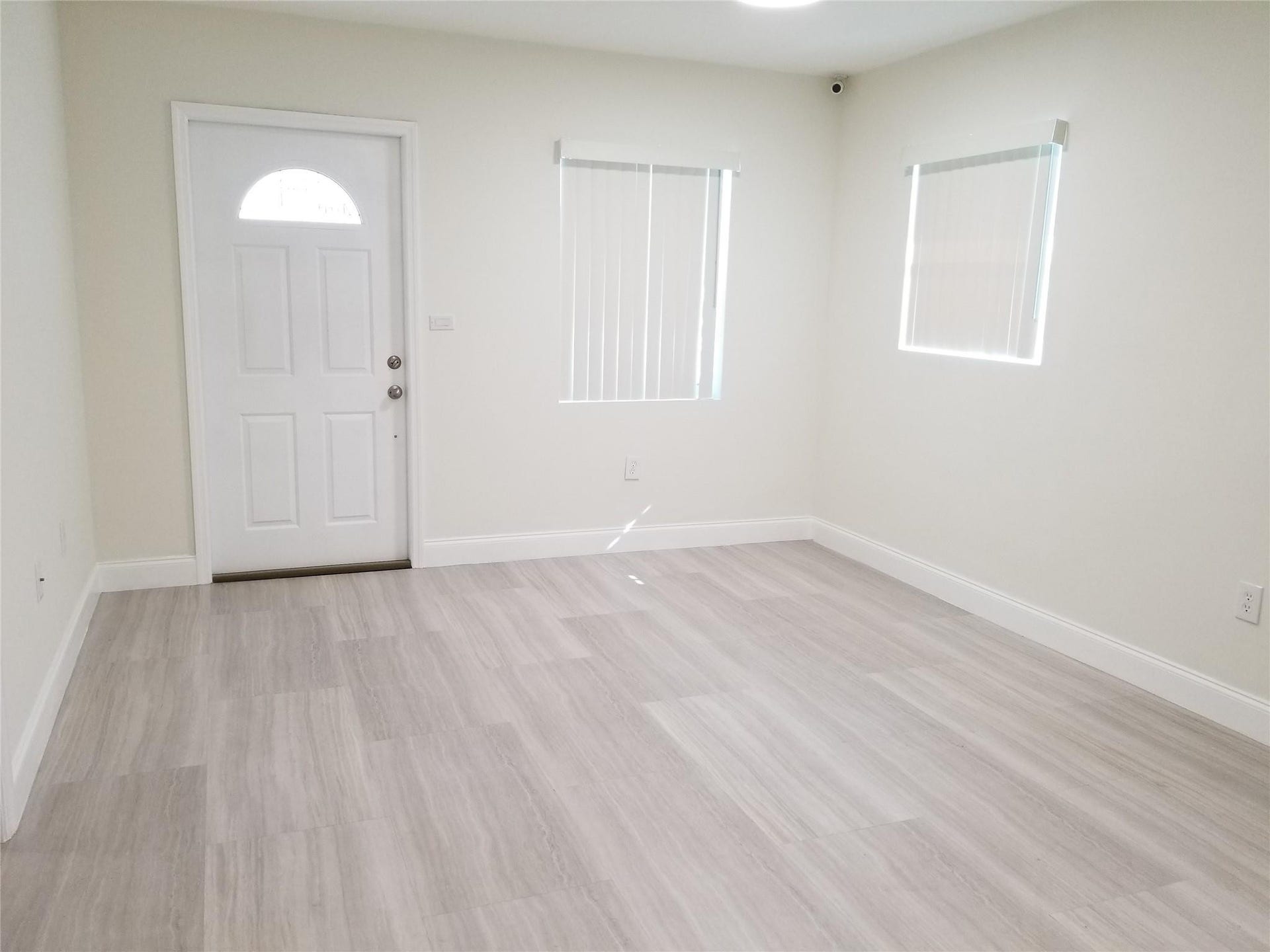 Light-toned wood-finish flooring, white paneled door with an arched lite, multiple windows with blinds, and recessed ceiling lighting