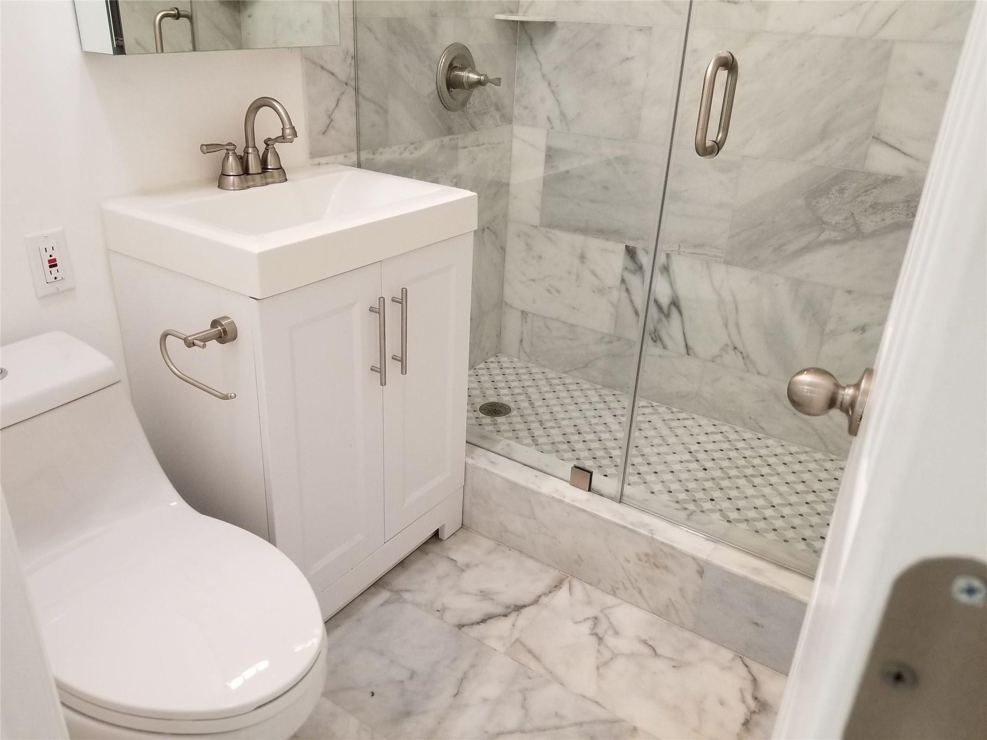 White vanity with brushed nickel hardware, walk-in shower with glass enclosure, white square vessel sink, and marble-finish tile flooring