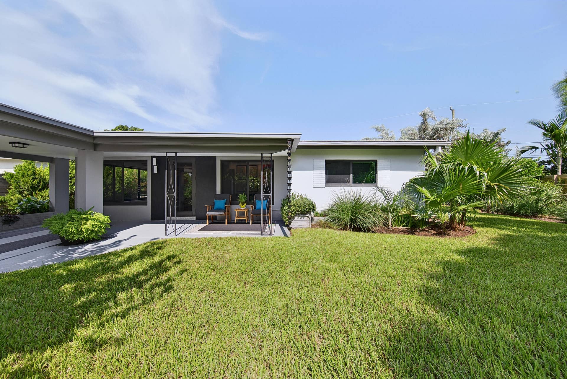 4850 NE 5TH Avenue, Oakland Park, FL 33334 Expansive lawn with mature landscaping, covered patio with recessed lighting, and a modern exterior design