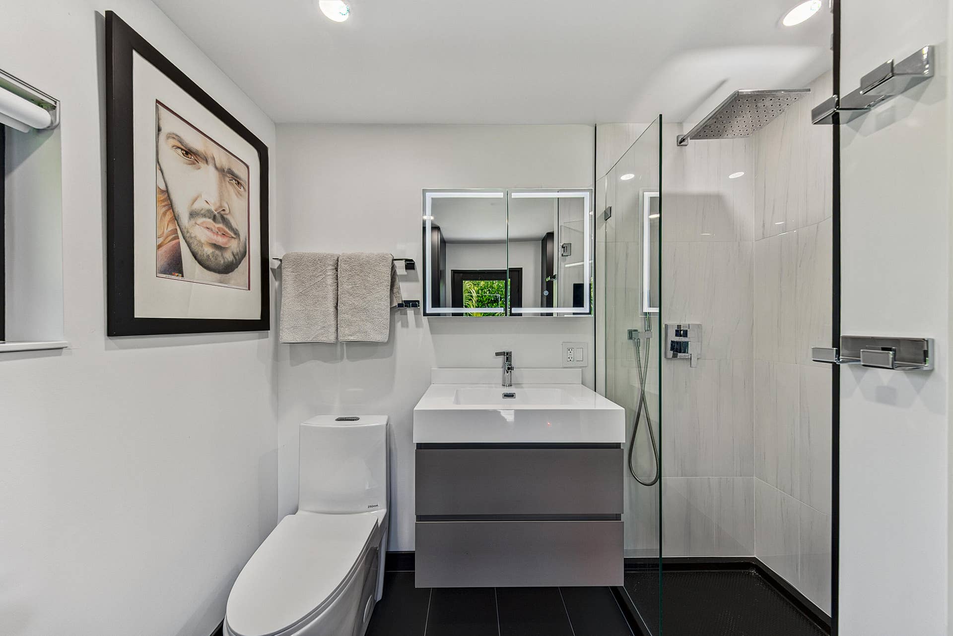4850 NE 5TH Avenue, Oakland Park, FL 33334 Second bath has a modern floating vanity with integrated sink, mirrored medicine cabinet with lighting, frameless glass shower enclosure, and a rainfall showerhead