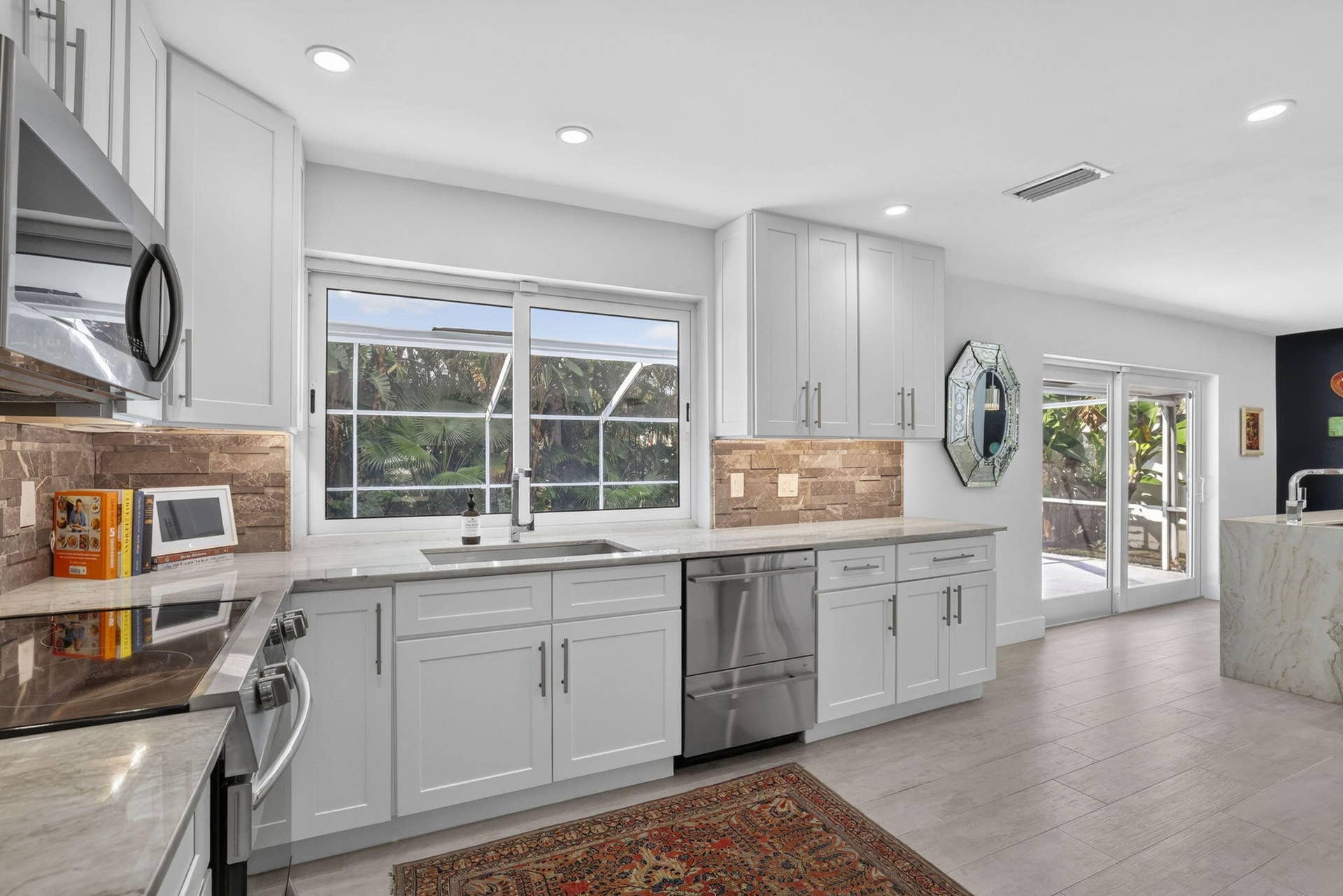 White shaker cabinetry, stone backsplash, stainless steel appliances, light-toned flooring, and sliding glass doors
