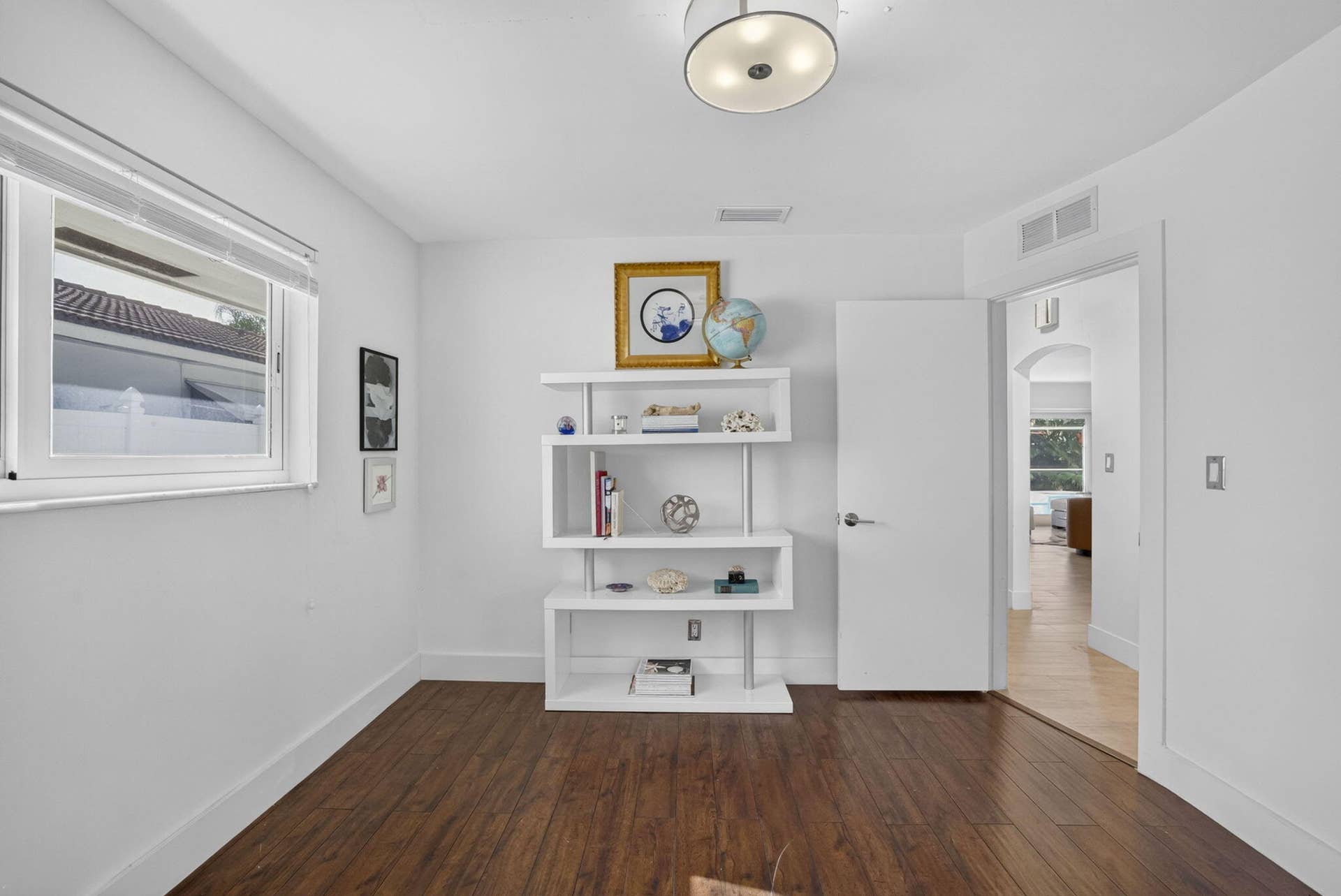 Window with blinds, wood-finish flooring, built-in shelving, white walls, and a semi-flush mount ceiling light