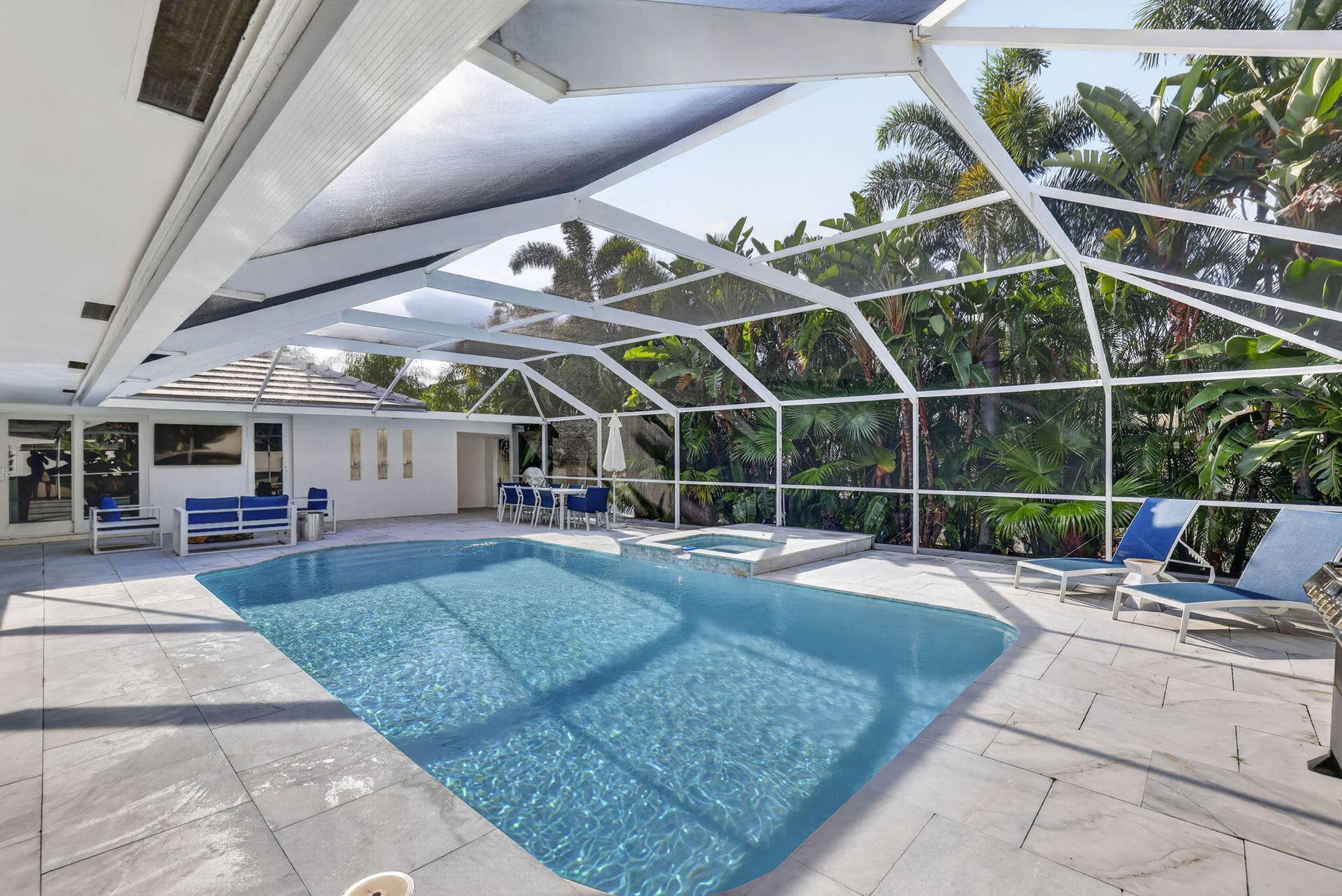 Screened-in pool area featuring a rectangular swimming pool, integrated spa, and expansive patio with tile flooring