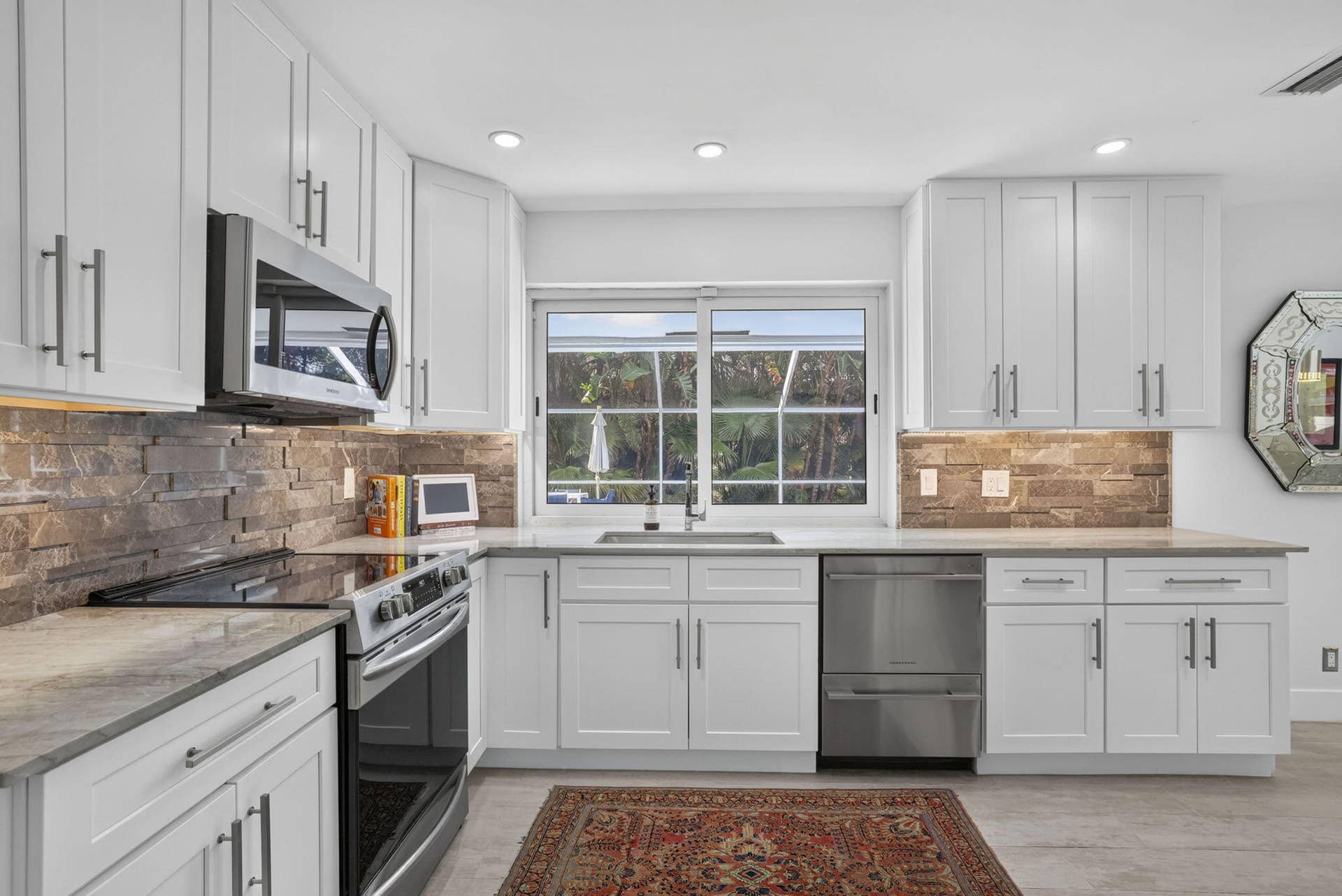 White shaker-style cabinetry, stainless steel appliances, stacked stone backsplash, light-toned countertops, and recessed lighting