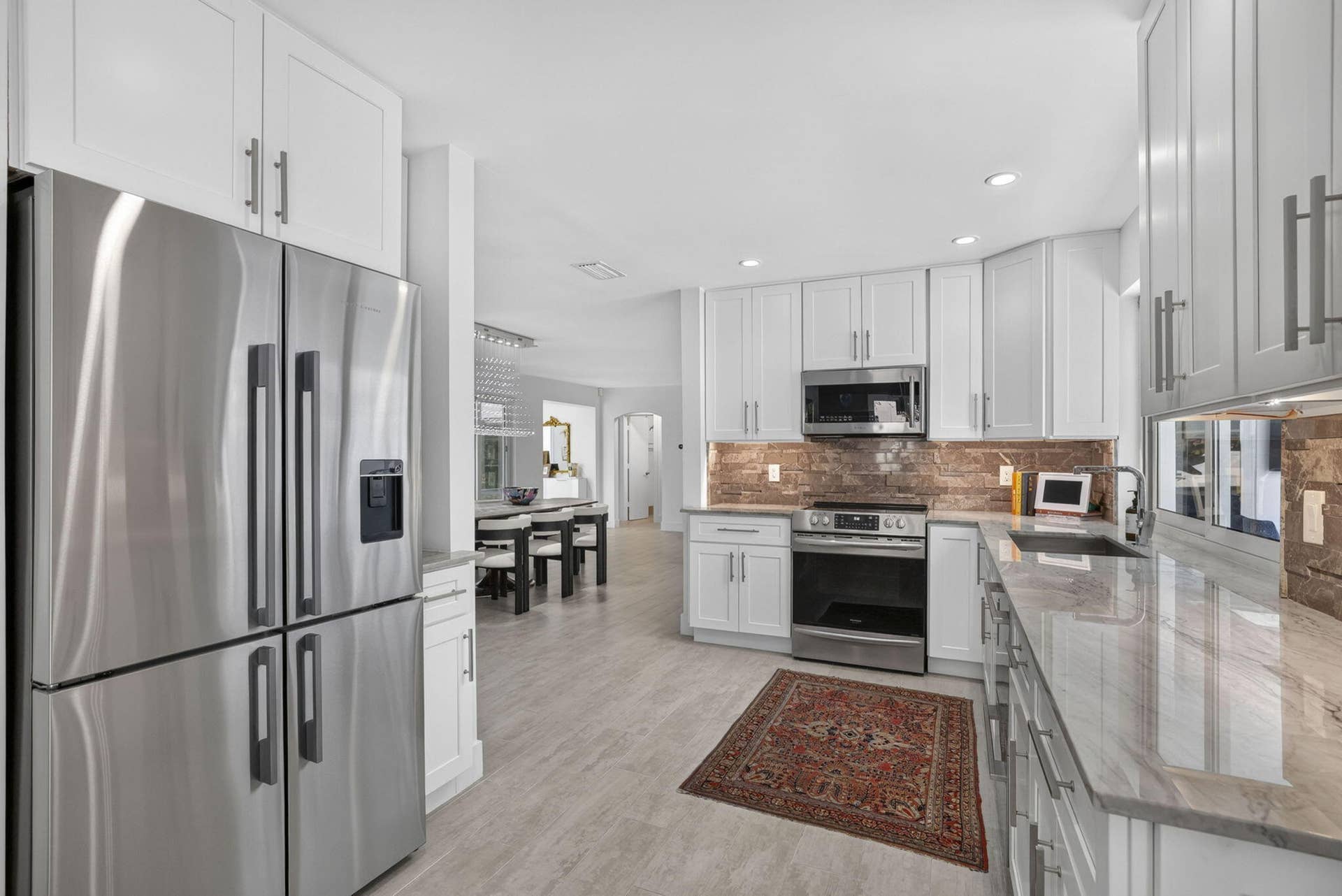 Stainless steel French door refrigerator, white shaker-style cabinetry, stainless steel appliances, stone backsplash, and light-toned countertop