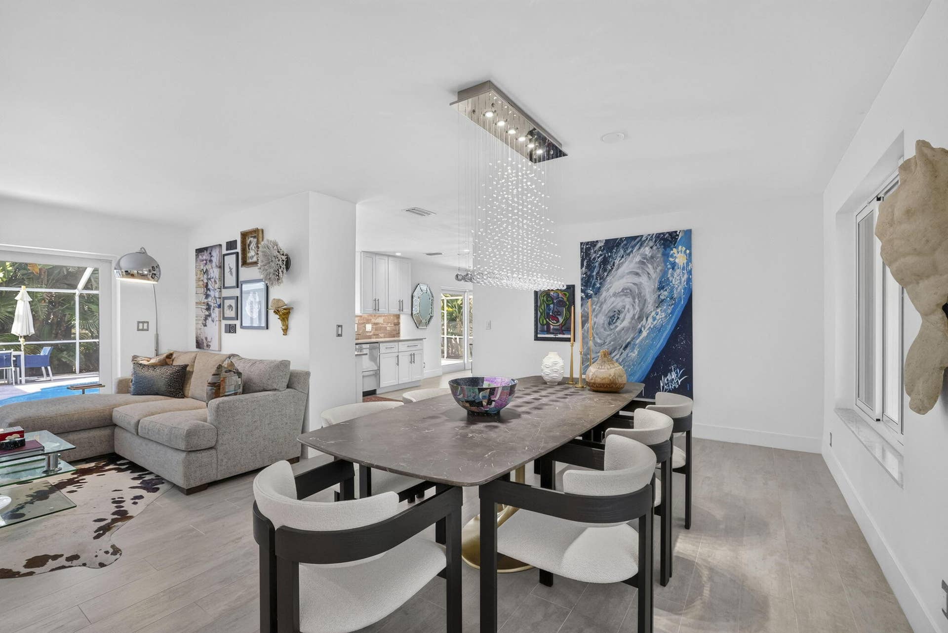 Open-concept living and dining area, a contemporary linear crystal chandelier, and a sliding glass door leading to an outdoor space