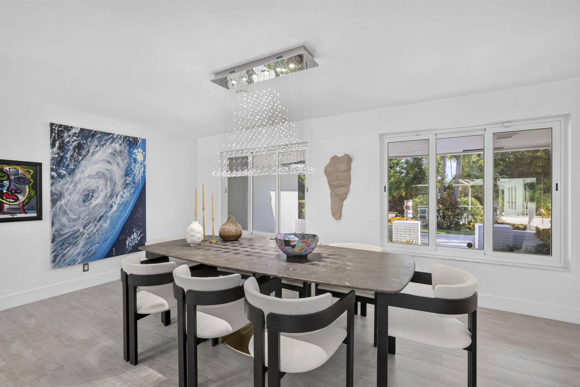 Expansive windows providing natural light, sleek tile flooring, and a contemporary linear chandelier with crystal accents