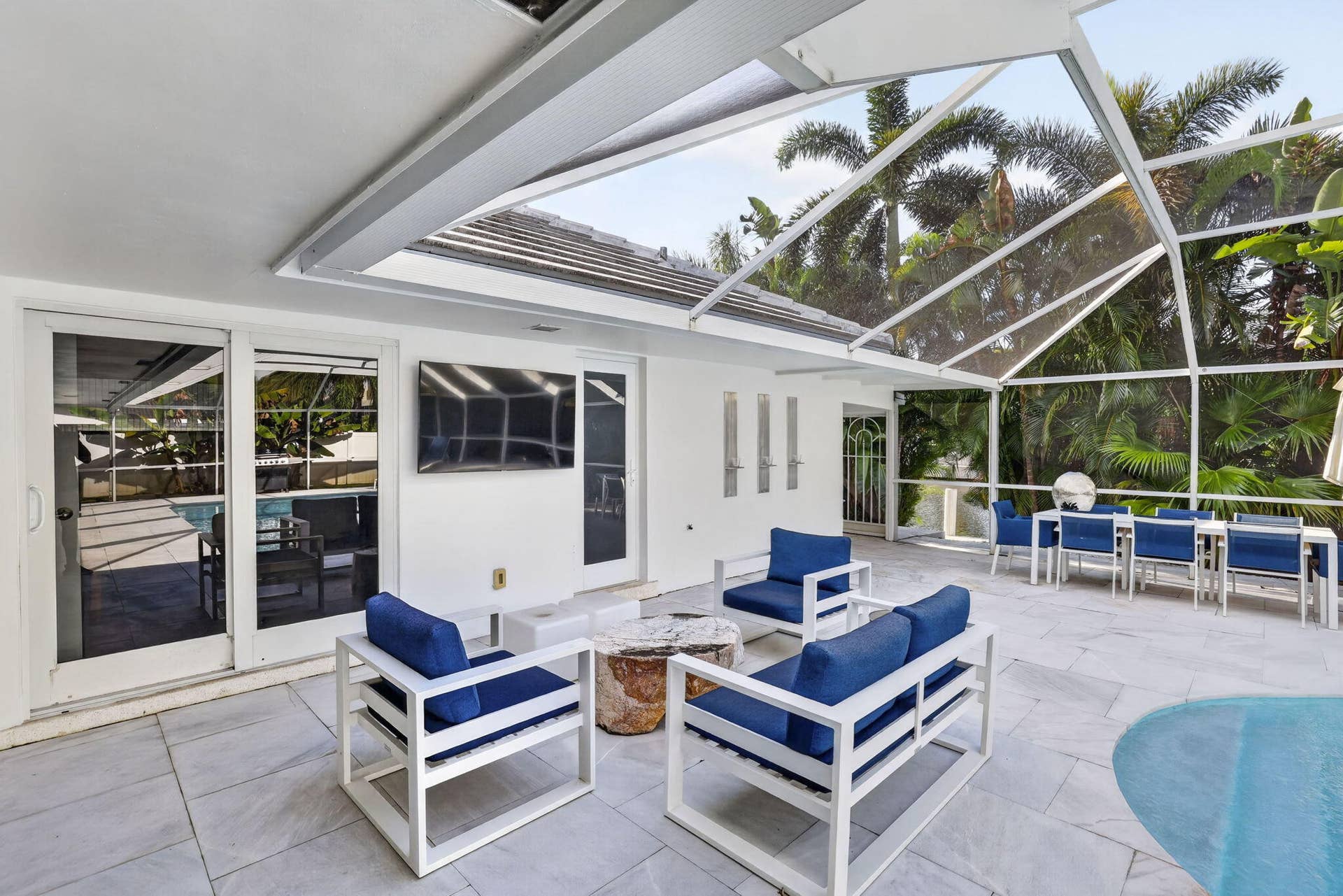 Screened outdoor living area with a stone tile patio, built-in pool, and tropical landscaping