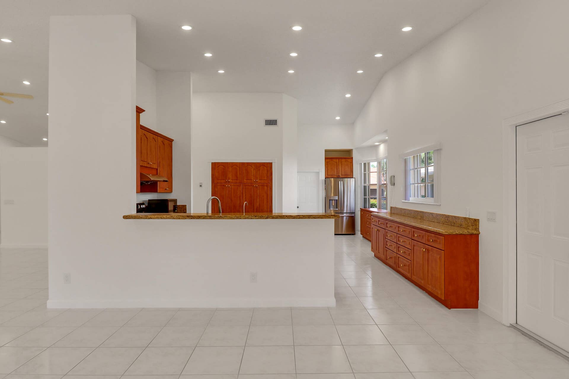 Kitchen and living area featuring white tile flooring, vaulted ceilings, recessed lighting, wood cabinetry, and stainless steel appliances