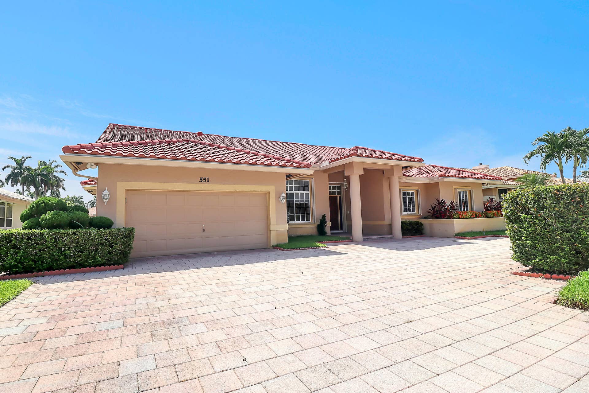 Mediterranean-style exterior featuring a clay tile roof, stucco finish, paver driveway, two-car garage, and established landscaping