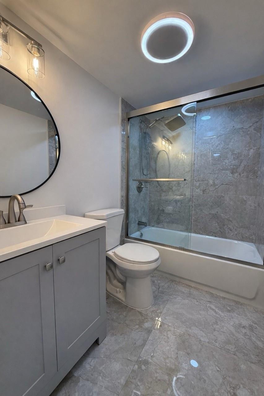 809 W Oakland Park Boulevard, #K4, Wilton Manors, FL 33311 Vanity with white countertop, round mirror, tile flooring, and a tub with glass sliding doors