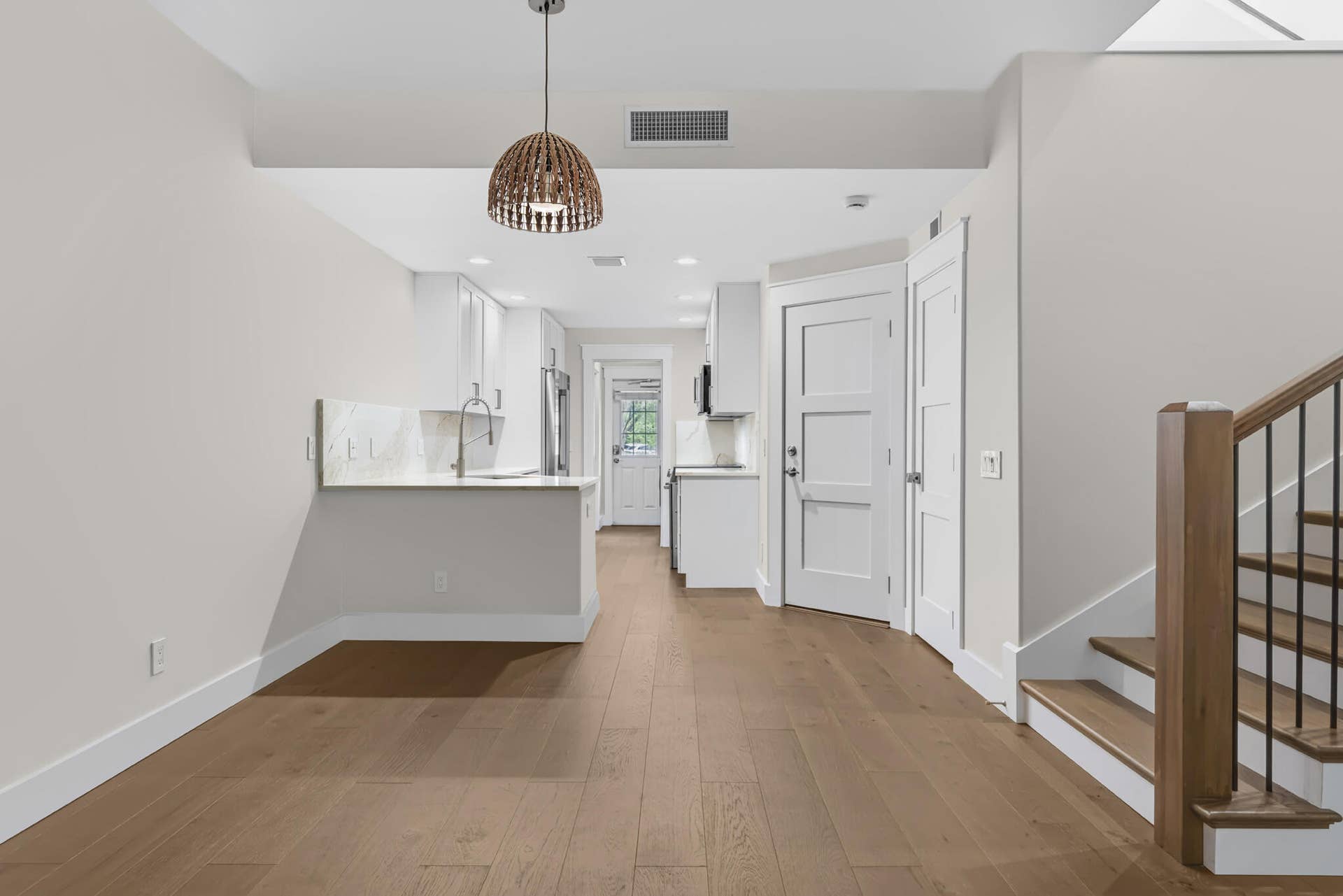 3207 E Community Drive E, Jupiter, FL 33458 Open-concept living area featuring wood-finish flooring, a contemporary kitchen with white cabinetry and light-toned countertops, and a staircase with wood treads and a black metal railing