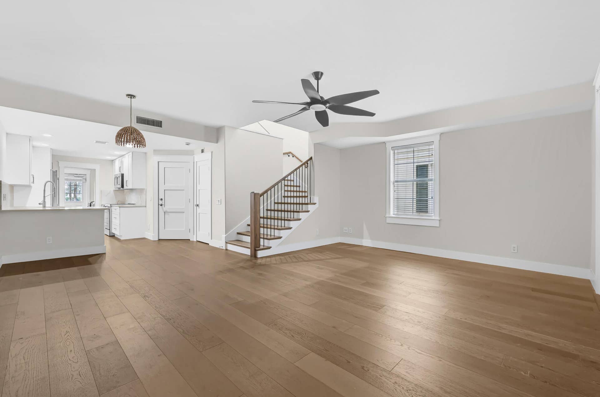 3207 E Community Drive E, Jupiter, FL 33458 Expansive open-concept living area featuring wood-finish flooring, a modern ceiling fan, and a staircase with wood treads and a metal railing