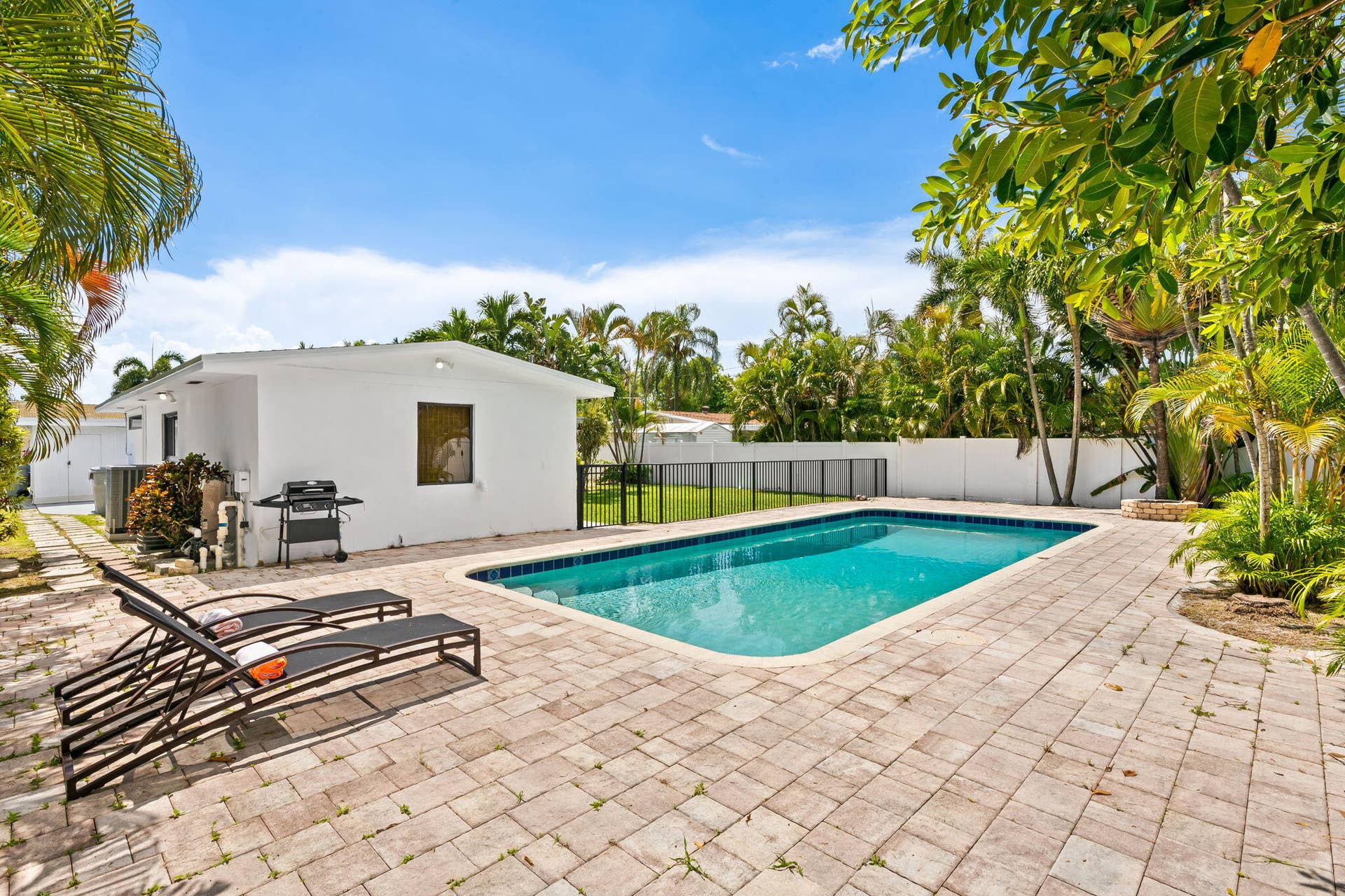 Rectangular swimming pool surrounded by a paver patio and lush tropical landscaping