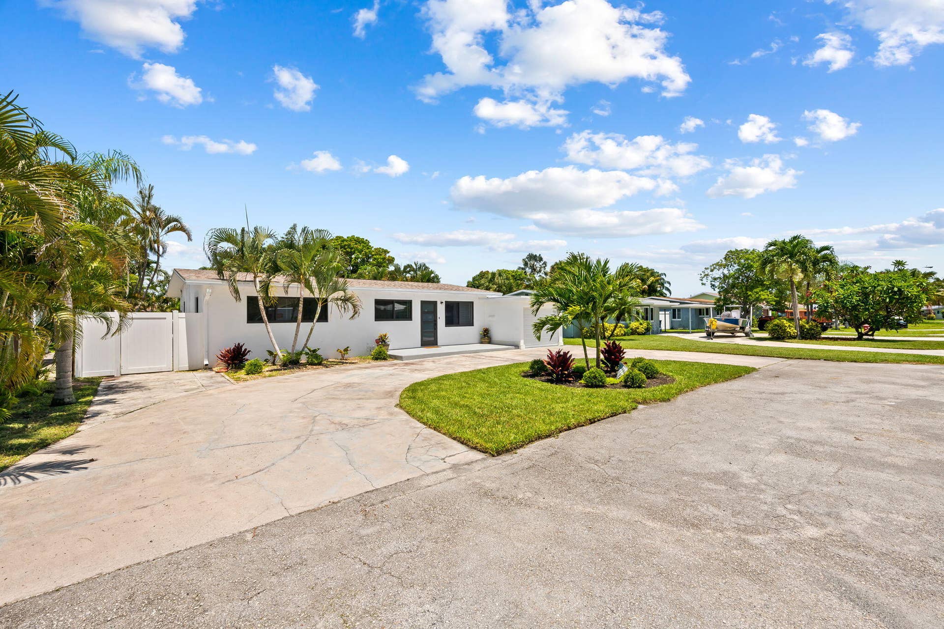 White exterior with black-framed windows, surrounded by mature palm trees and landscaped planting beds