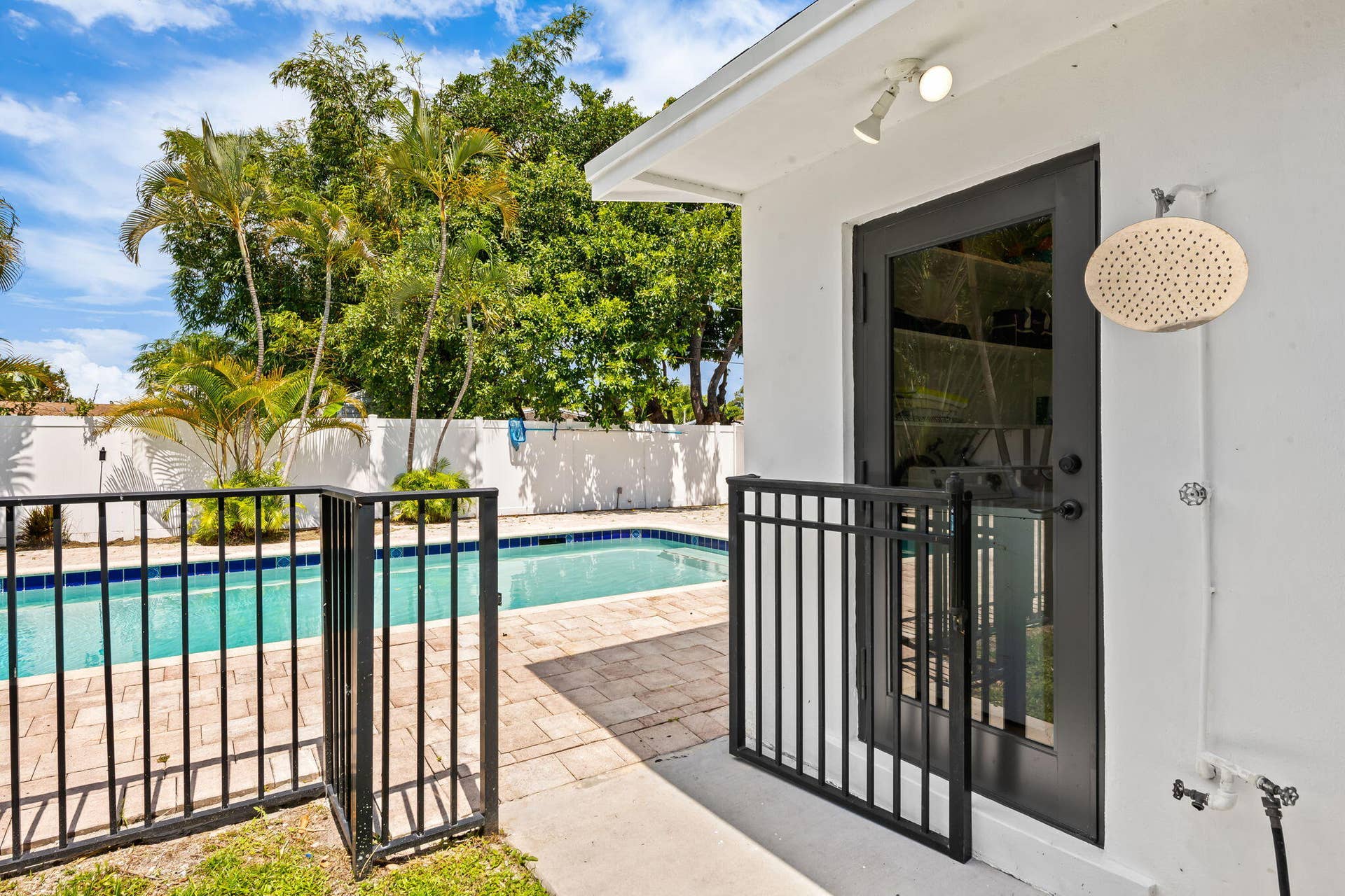 Backyard oasis featuring a resort-style saltwater pool with sun deck, black aluminum safety fencing, mature tropical landscaping, and direct access from the home via glass sliding doors