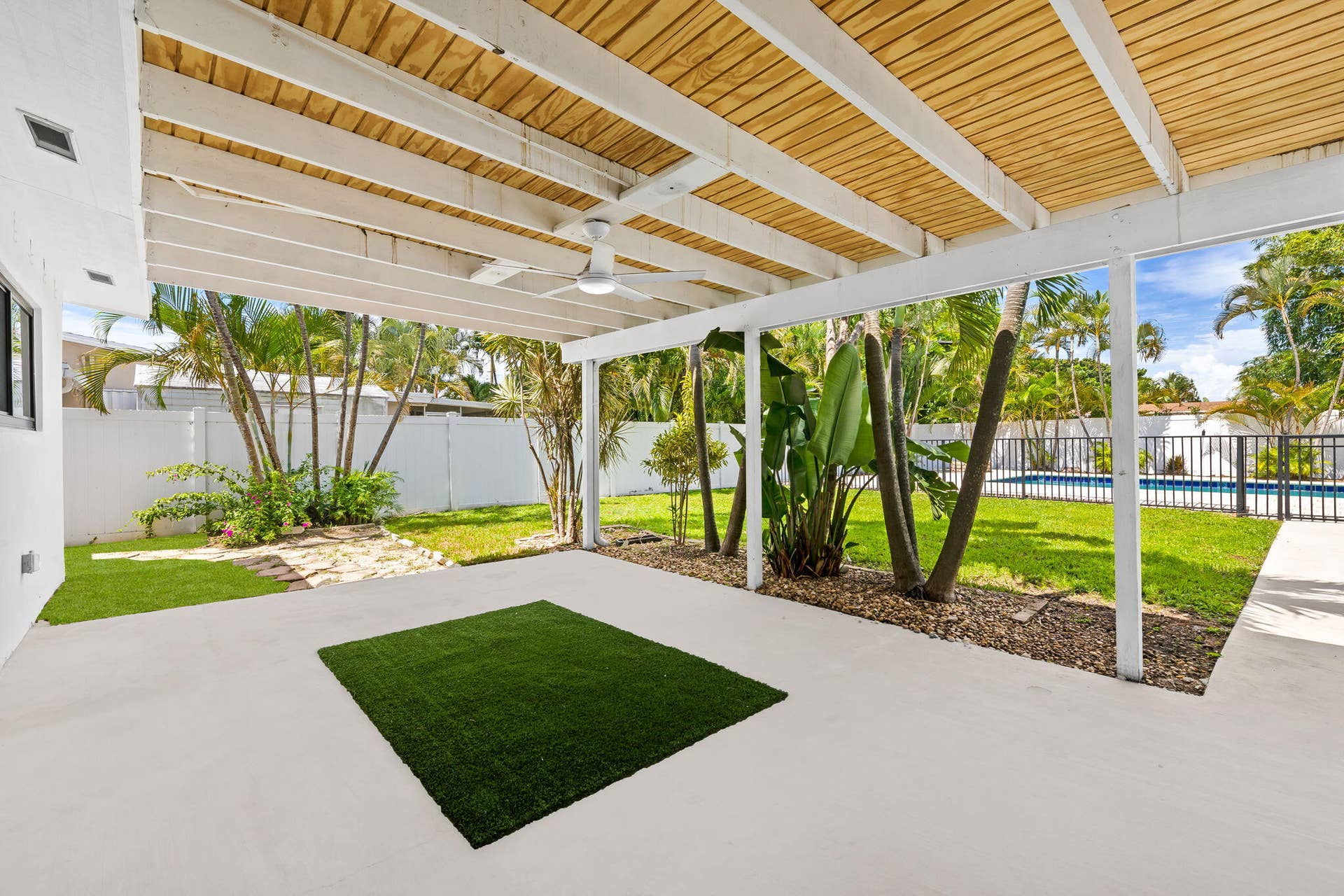 Covered patio with a ceiling fan, white support beams, and exposed wood ceiling planks